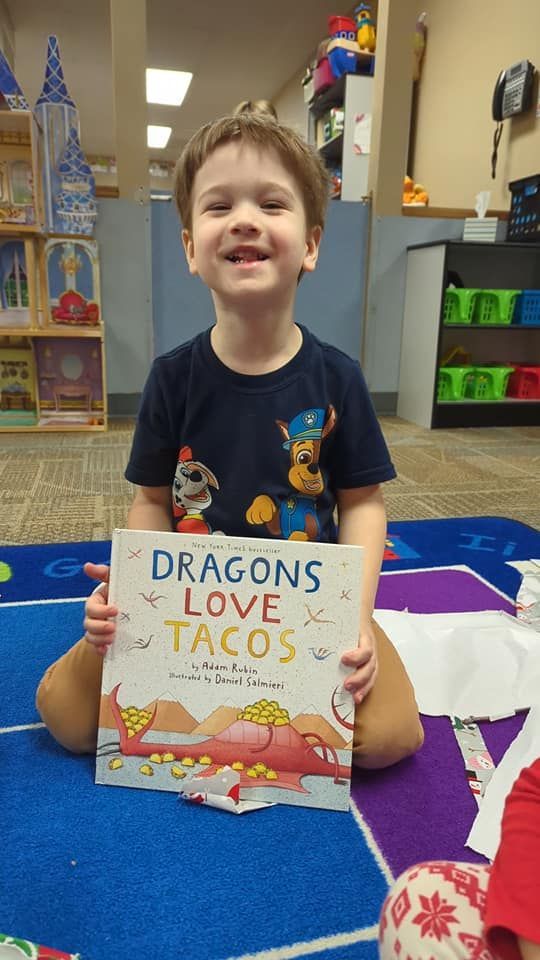 A young boy is sitting on the floor holding a book titled dragons love tacos.