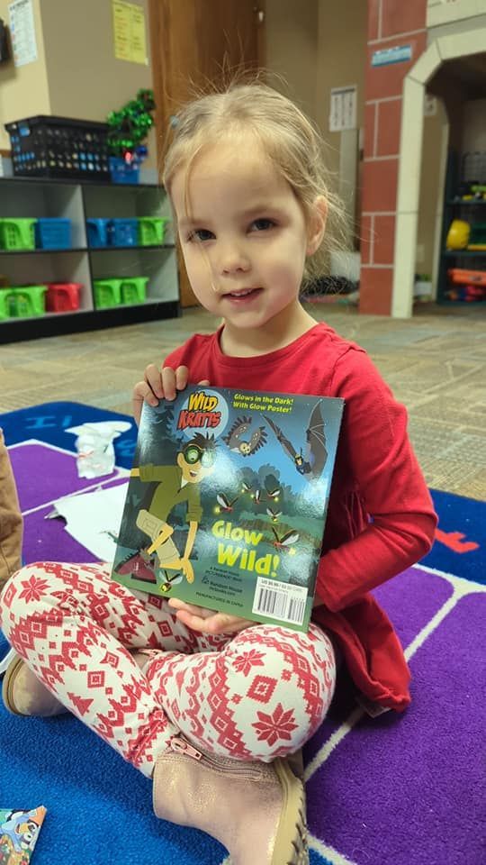 A little girl is sitting on the floor holding a book.