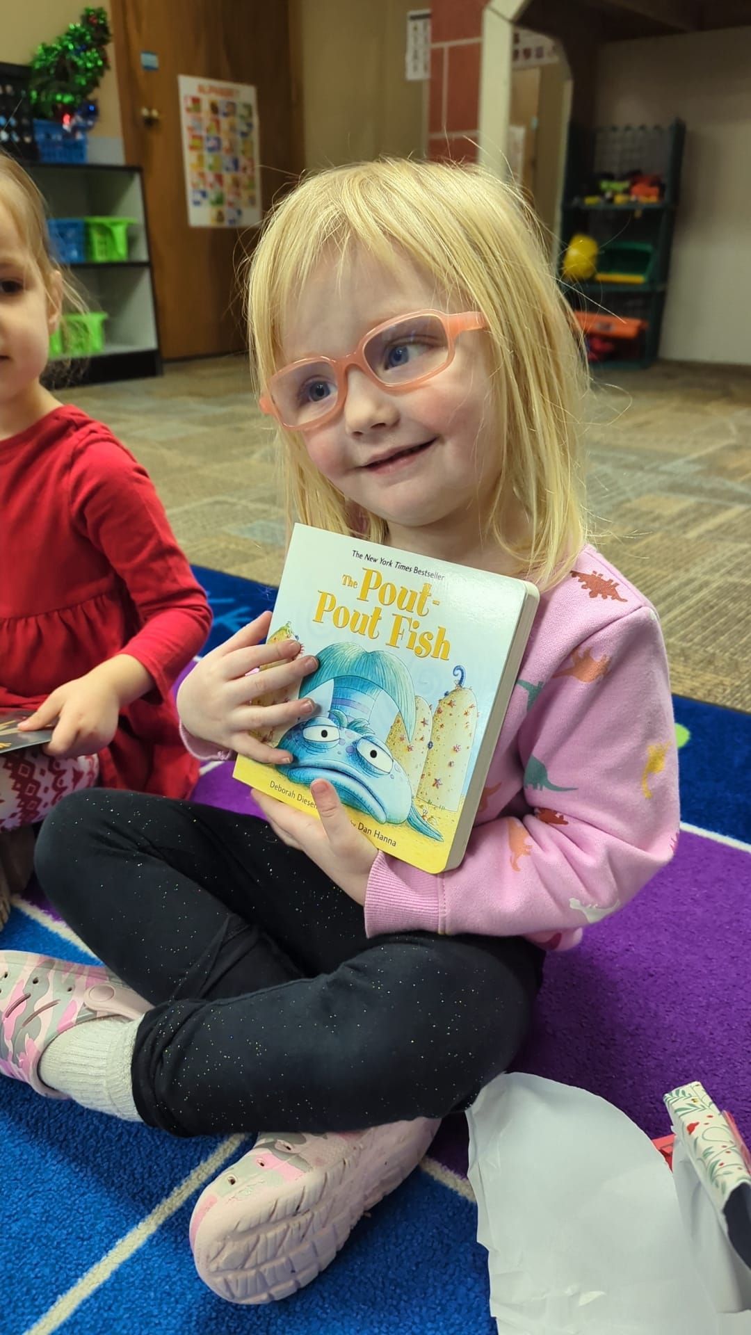 A little girl is sitting on the floor holding a book.