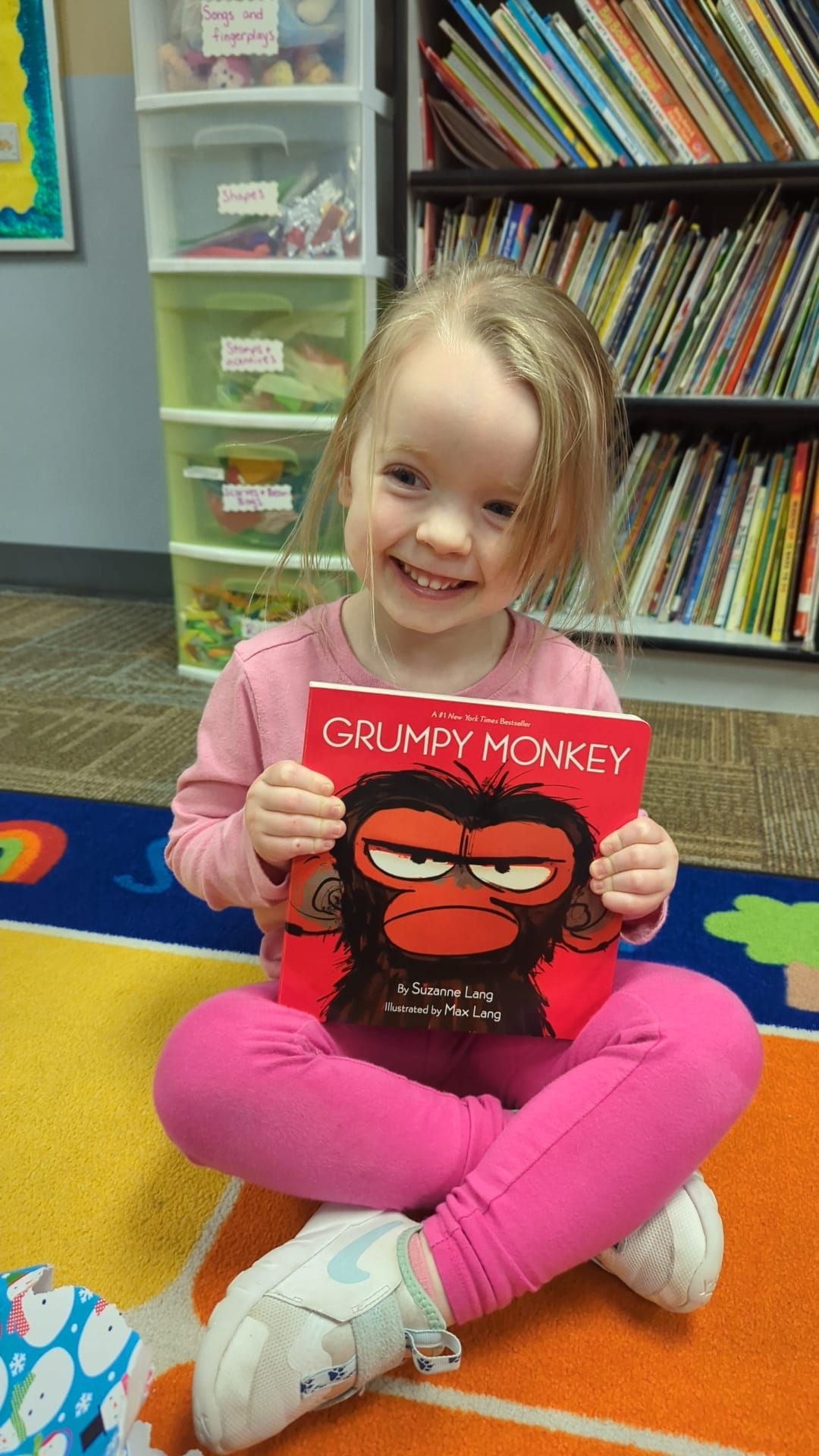 A little girl is sitting on the floor holding a book called grumpy monkey.