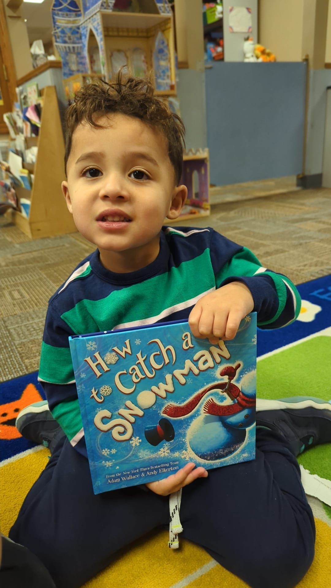 A young boy is sitting on the floor holding a book about how to catch a snowman.