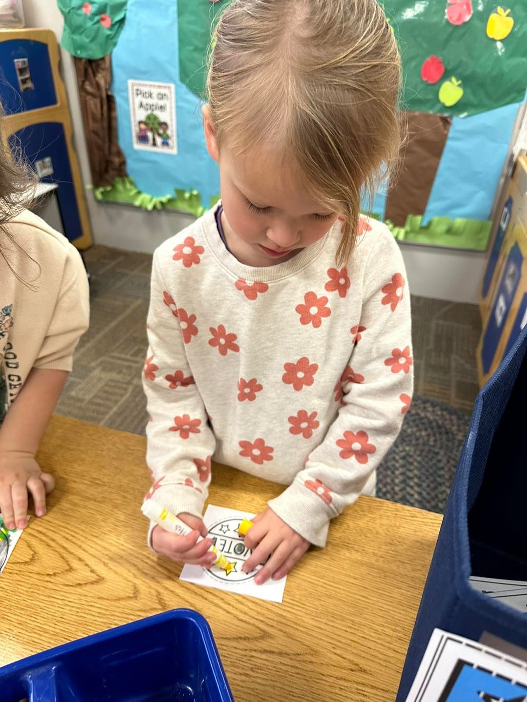A little girl is sitting at a table drawing on a piece of paper