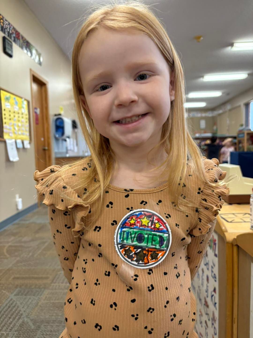 A little girl wearing a brown shirt is smiling for the camera.