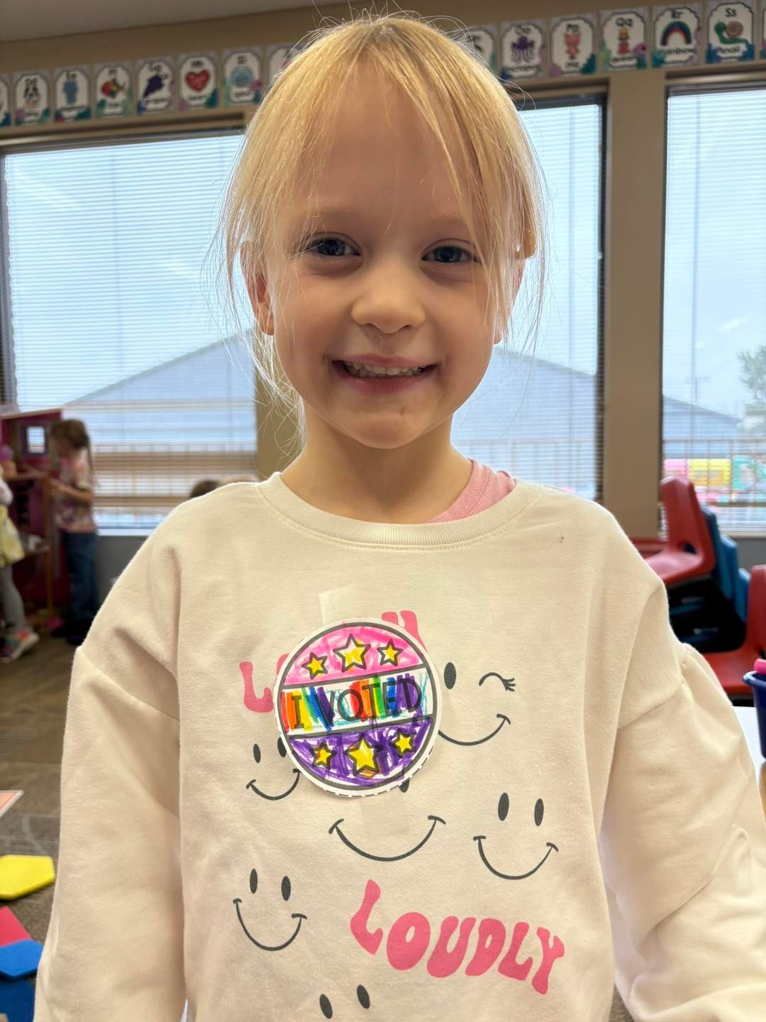 A little girl is wearing a white sweatshirt with smiley faces on it.