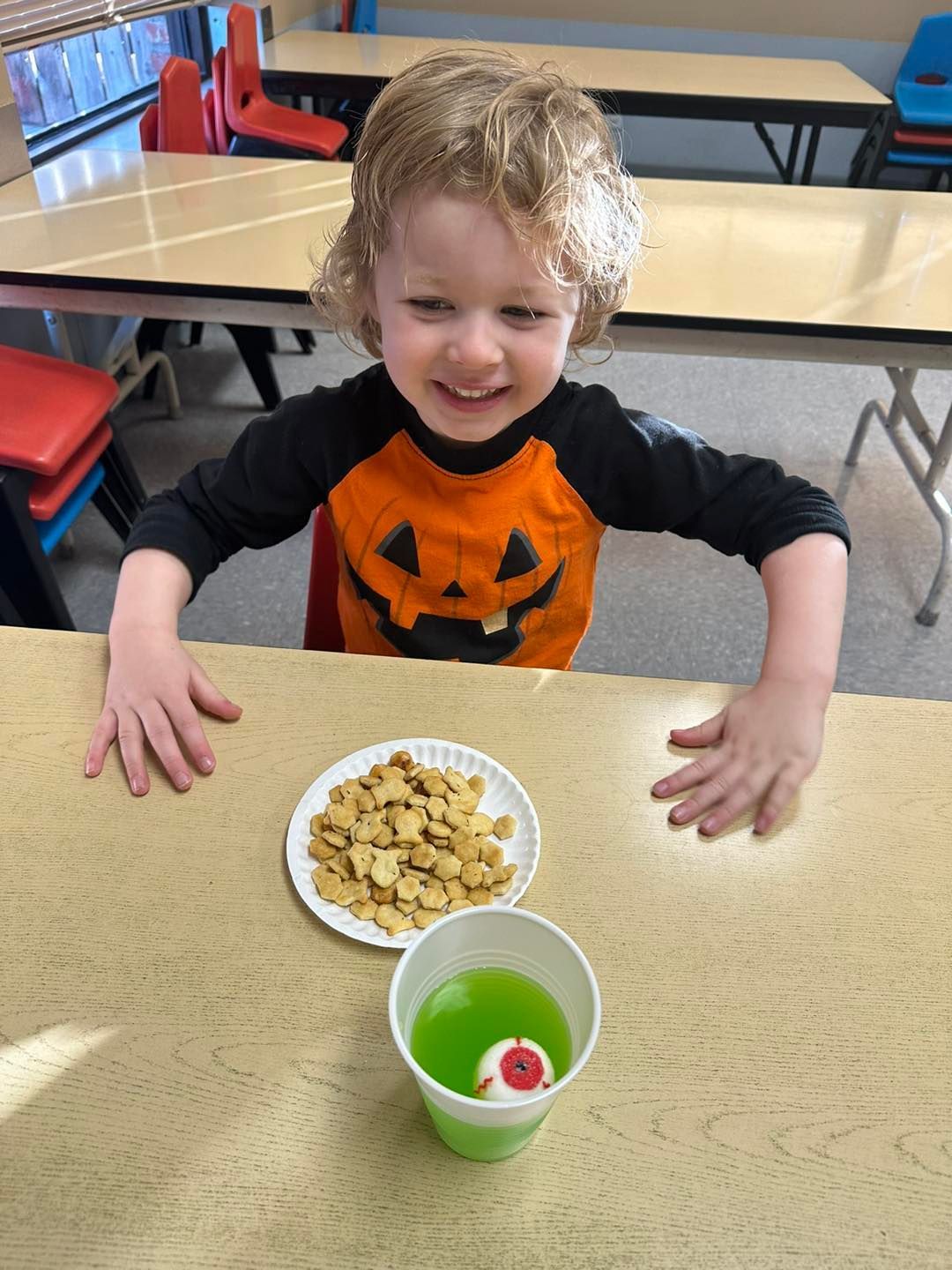 A young boy is sitting at a table with a plate of food and a cup of green liquid.