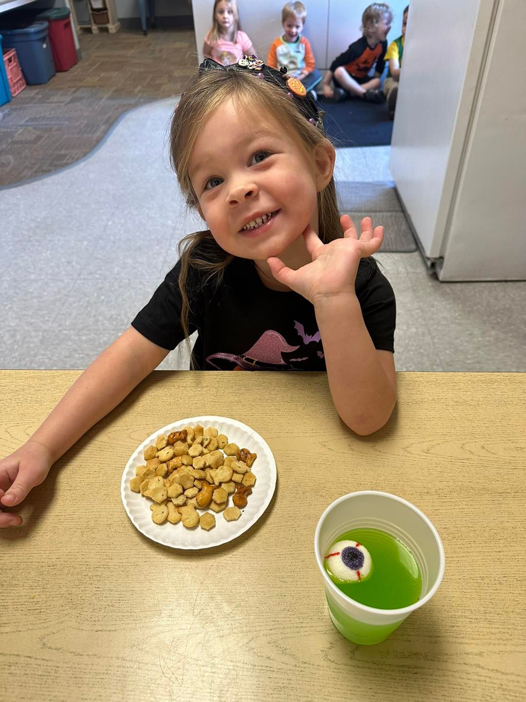 A little girl is sitting at a table with a plate of crackers and a cup of juice.