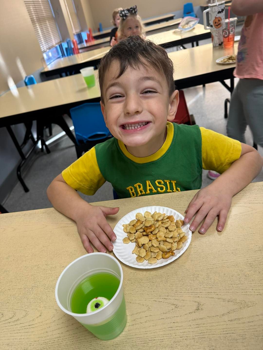 A young boy is sitting at a table with a plate of food and a cup of green liquid.