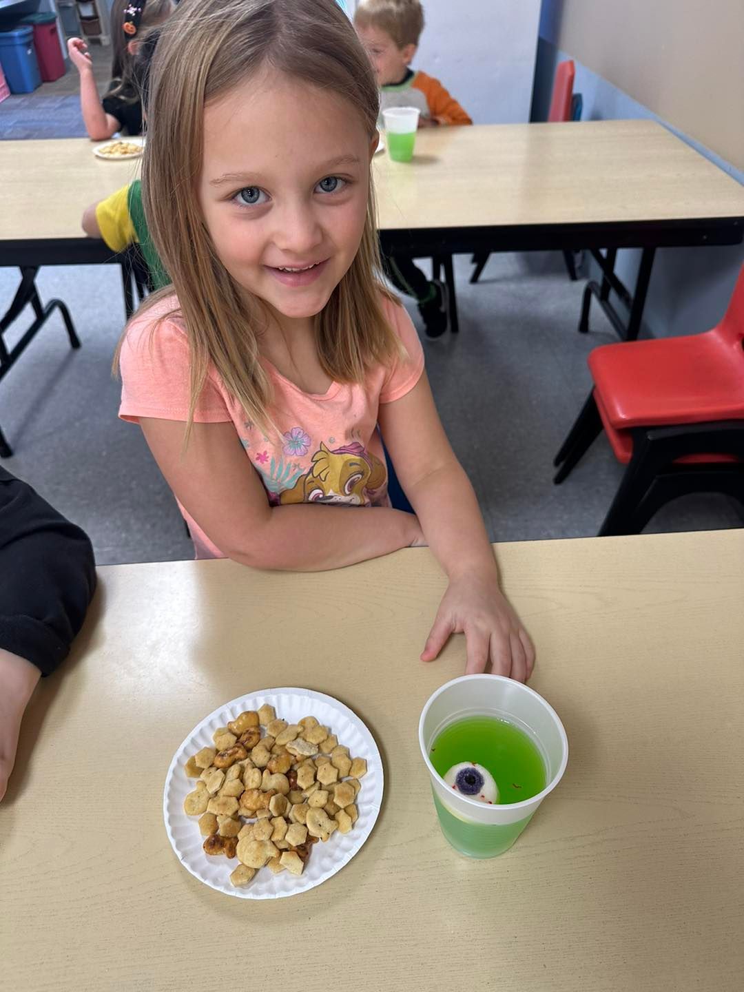 A little girl is sitting at a table with a plate of food and a cup of green liquid.