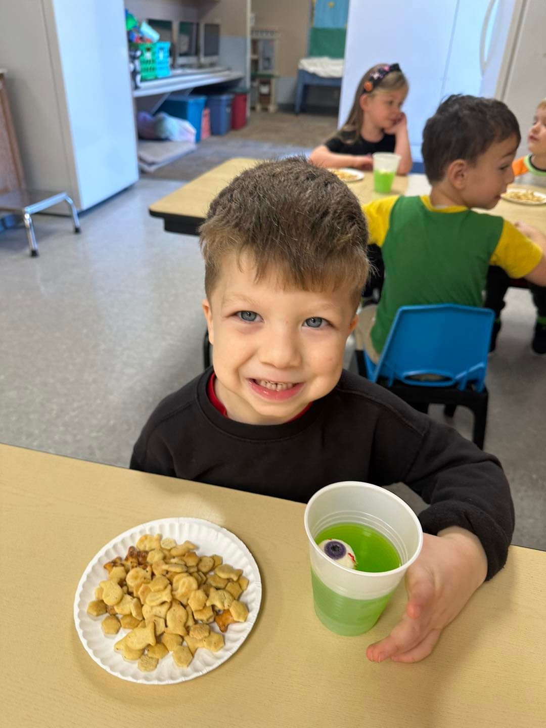 A young boy is sitting at a table with a plate of food and a cup of green liquid.