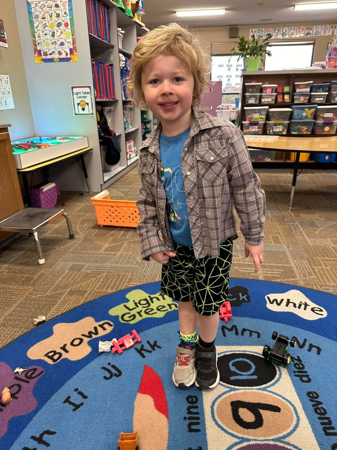 A young boy is standing on a rug in a classroom.
