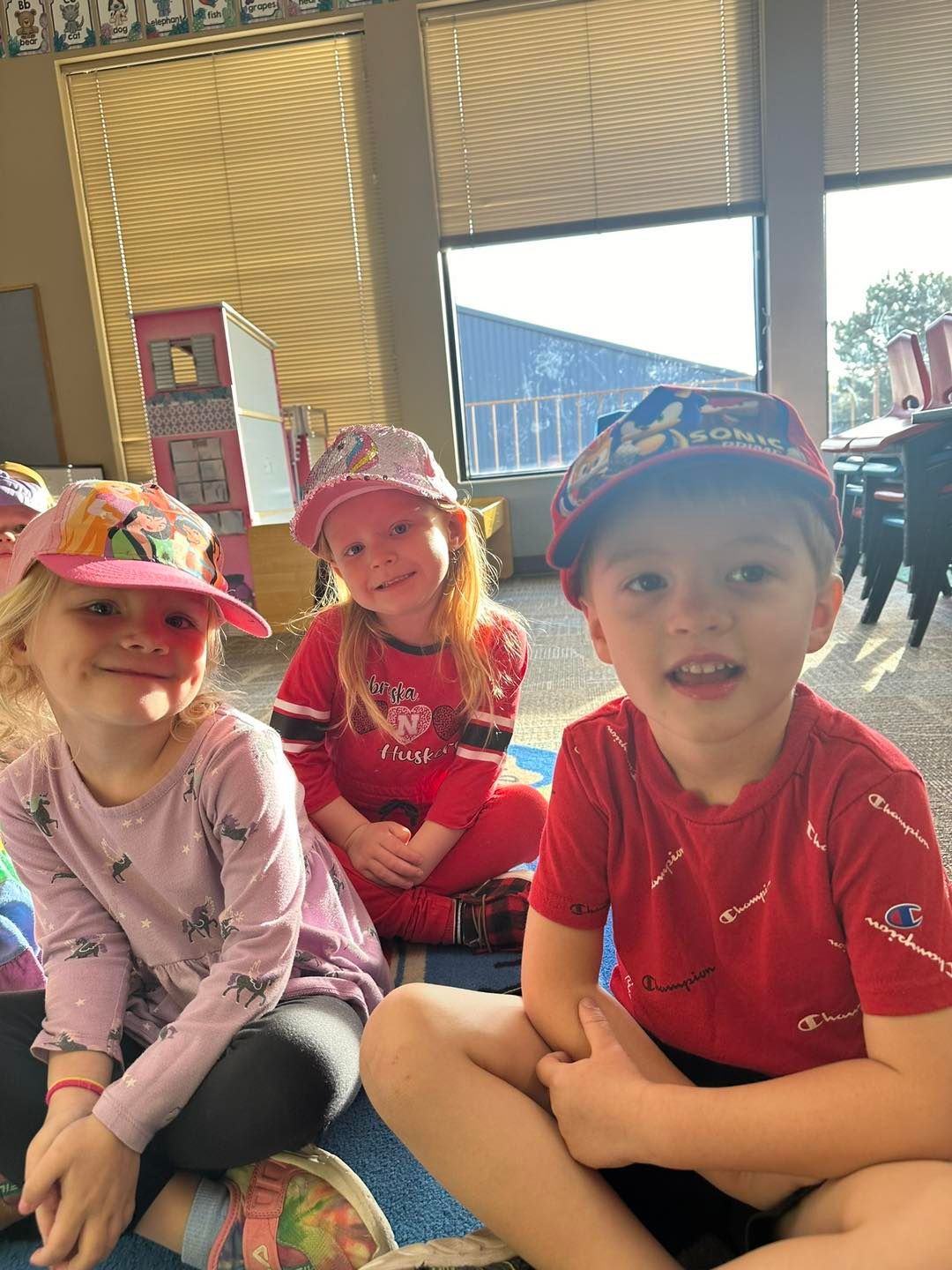 Three children are sitting on the floor wearing hats.