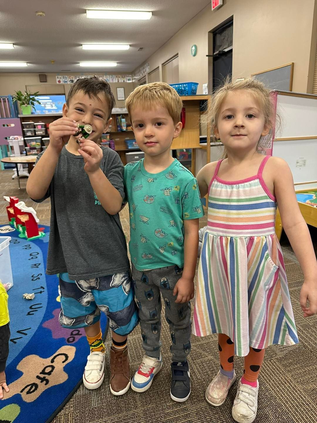 Three children are standing next to each other in a classroom.