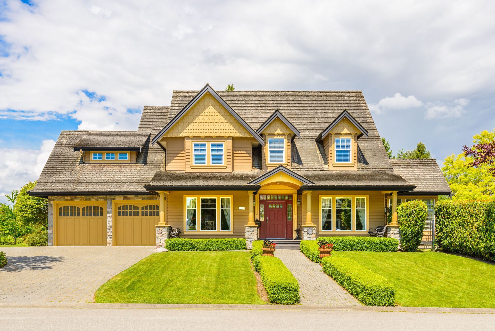Large two-story house with yellow siding, garage, and a manicured lawn with a pathway on a sunny day.