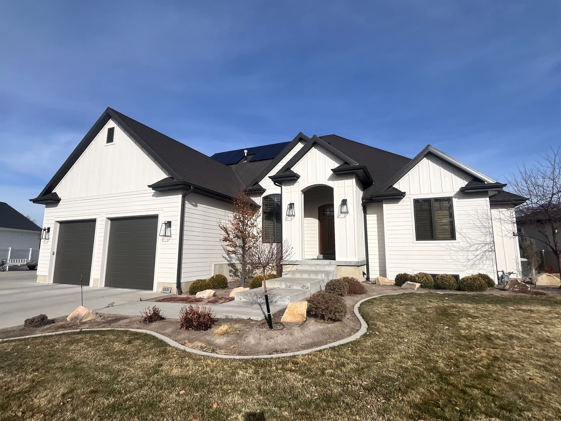 Modern white single-story house with dark roof, three garage doors, and landscaped front yard.