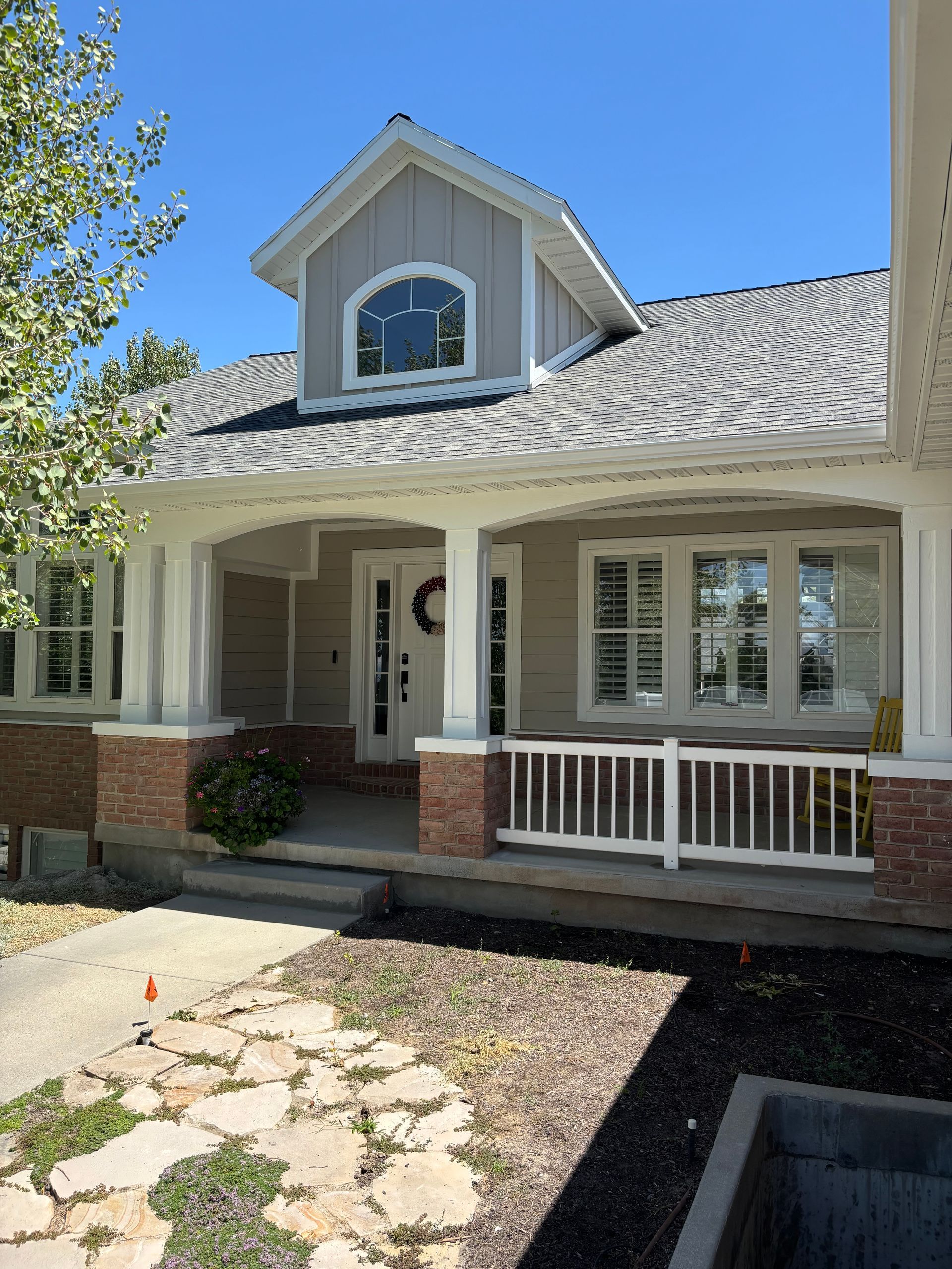 Tan house with porch, white columns, brick accents, and a dormer, blue sky background.