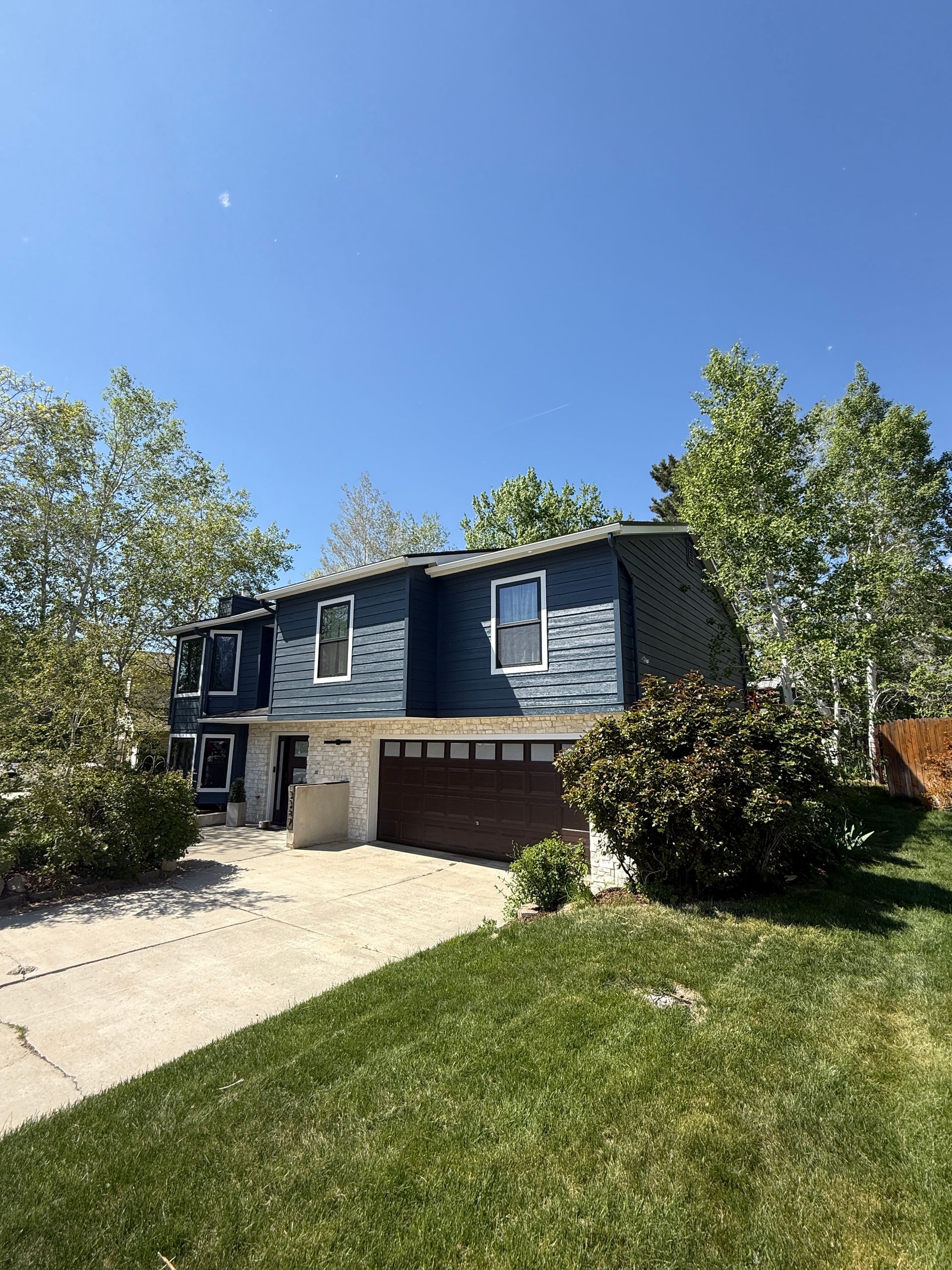 Blue house with a brown garage door and green lawn under a blue sky.