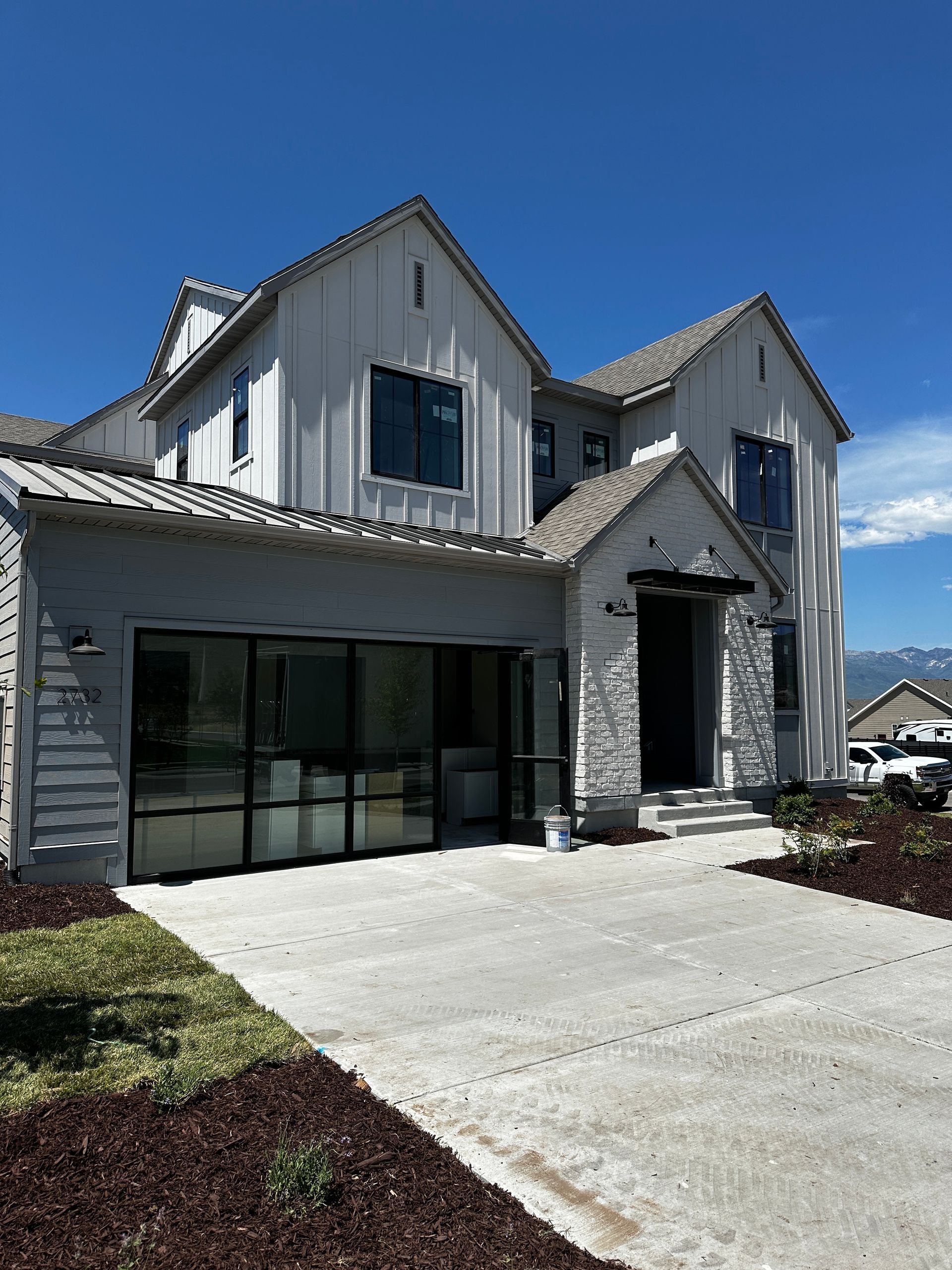 Two-story modern house with a glass garage door and a concrete driveway, on a sunny day.