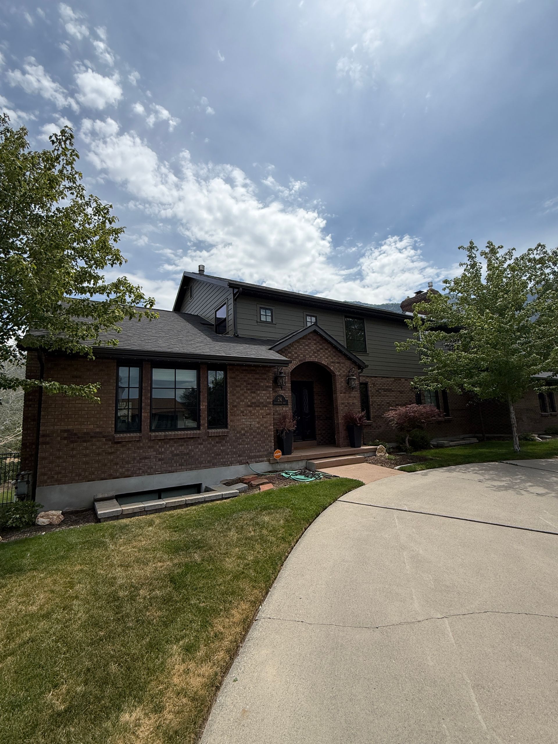 House with brick and green siding, driveway, and cloudy sky.