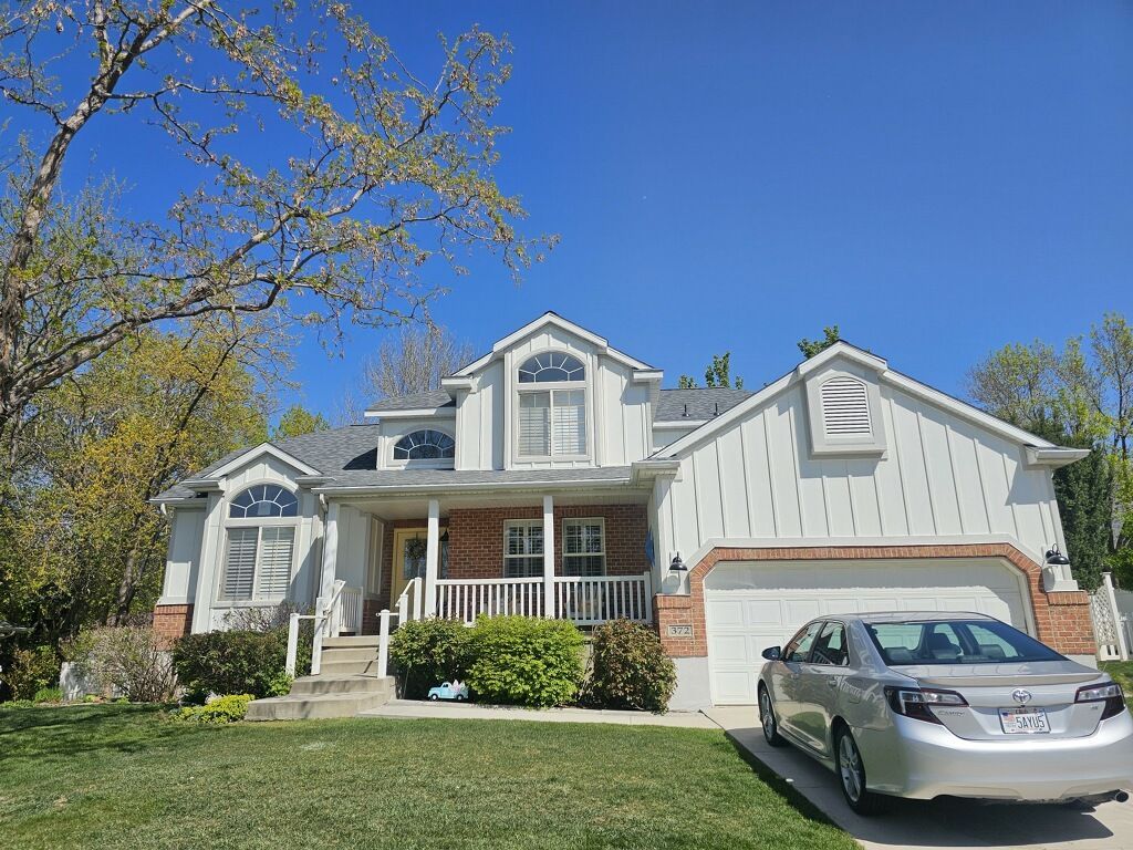 Two-story white house with a silver car in the driveway, green lawn, and a blue sky.
