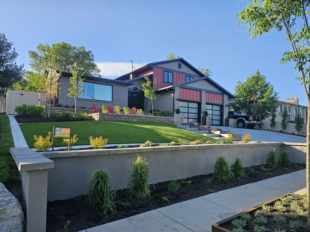 Modern house with red accents, brick exterior, and a well-manicured lawn behind a low wall.