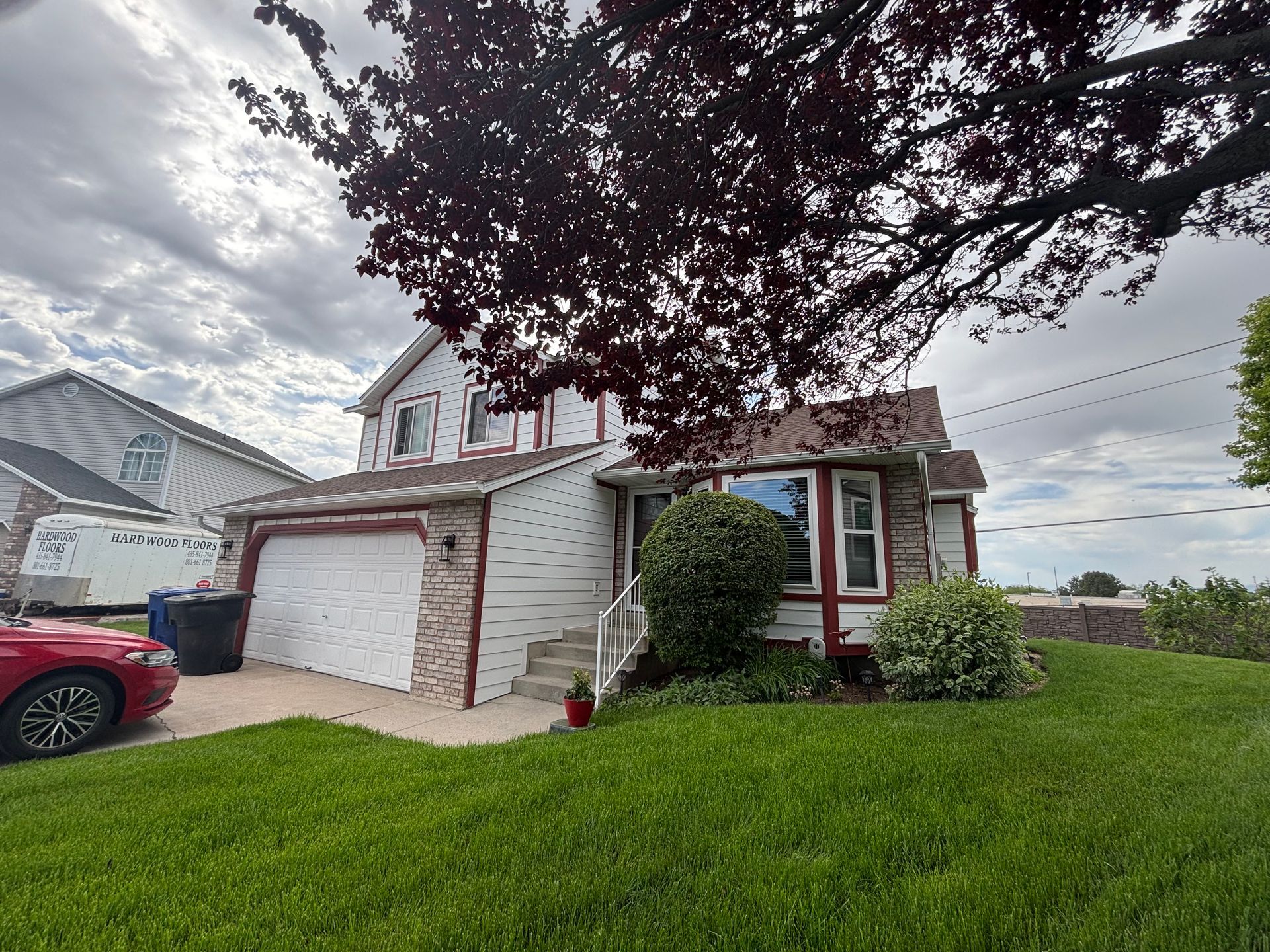 House with white siding, red trim, and a garage, with a red car in front.