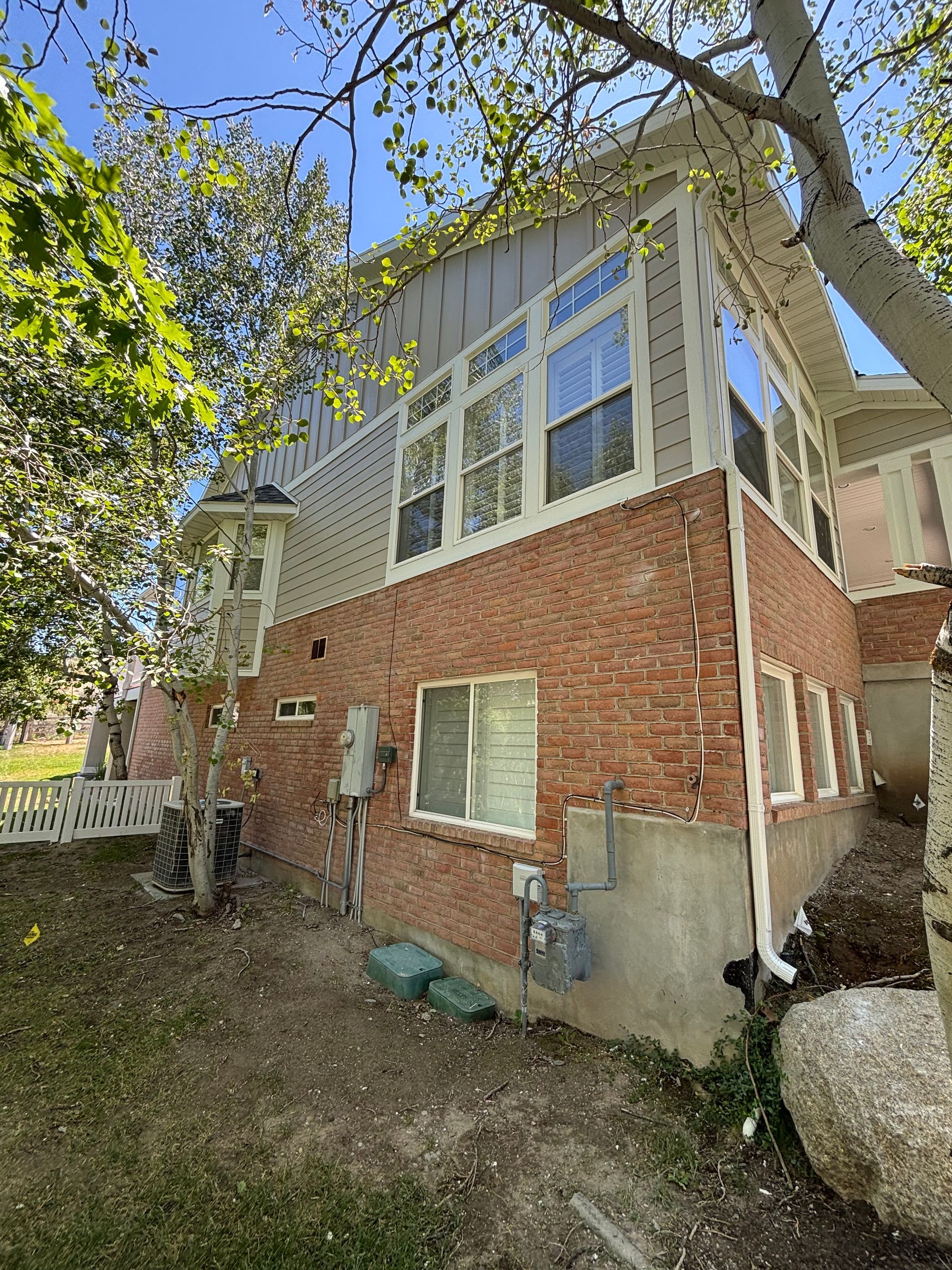 Brick and light siding house exterior with many windows, green trees, and a sunny sky.