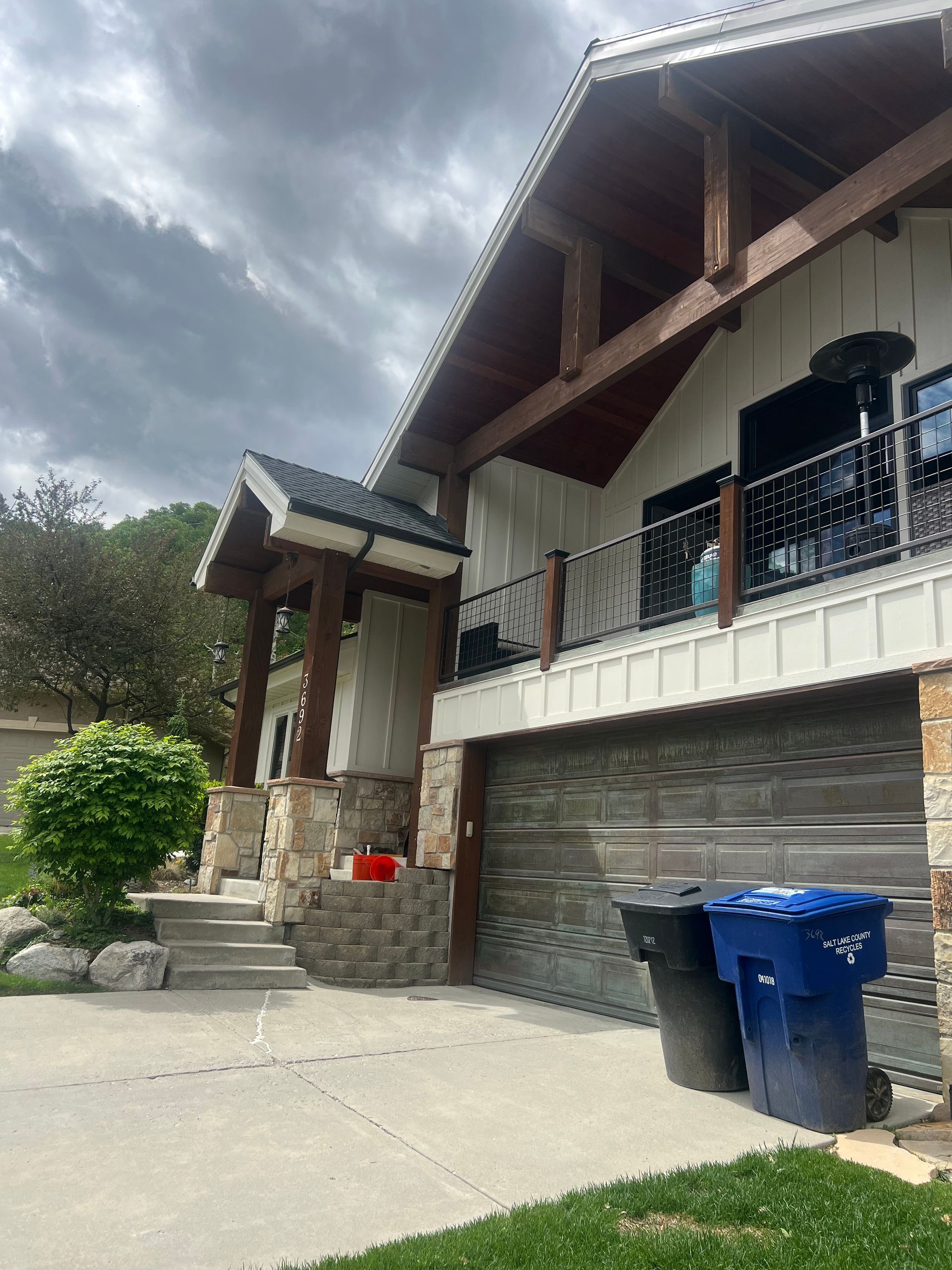 House exterior with garage, balcony, stone columns, and driveway; cloudy sky overhead.