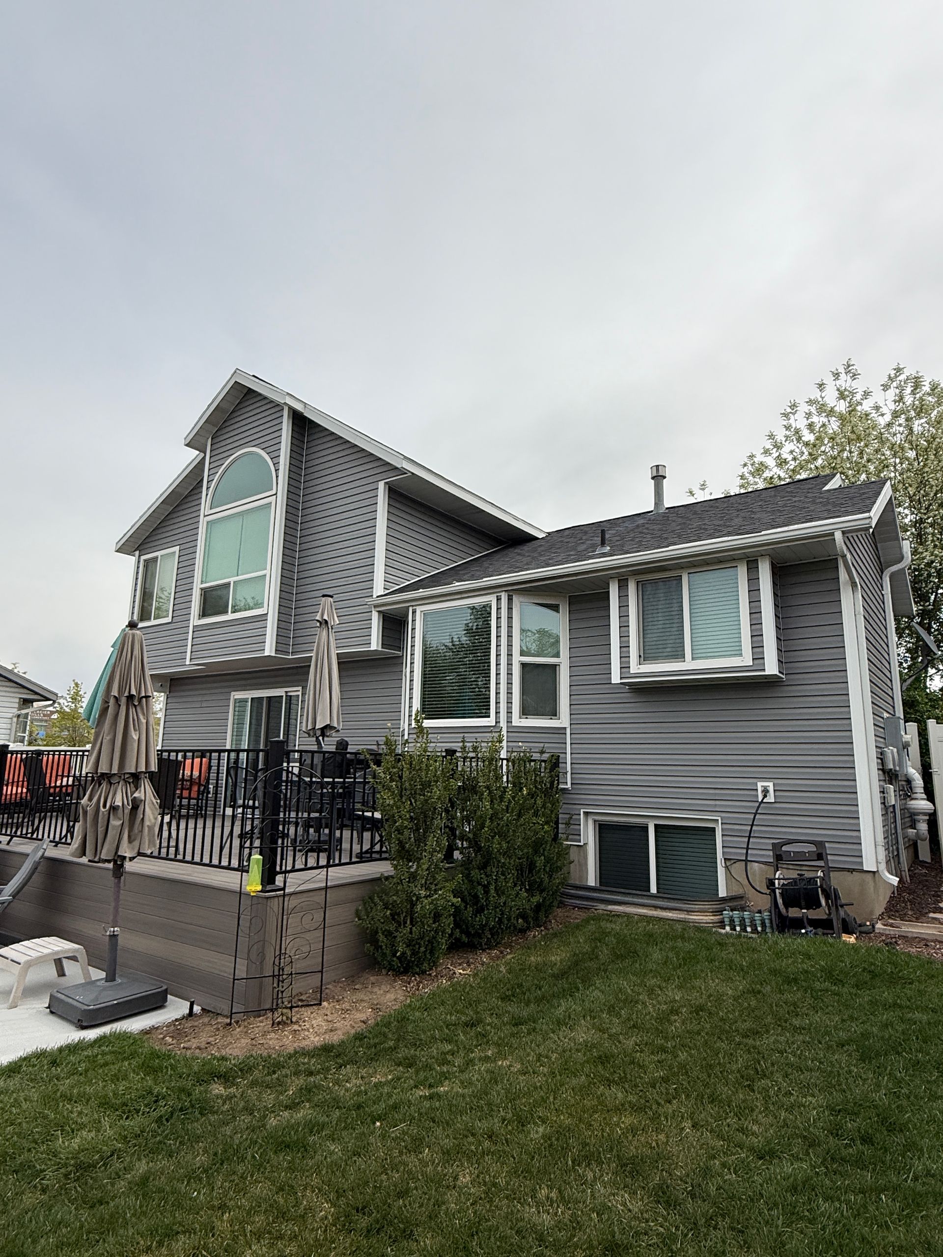 Gray house with multiple windows, a small deck, and green lawn. Overcast sky.