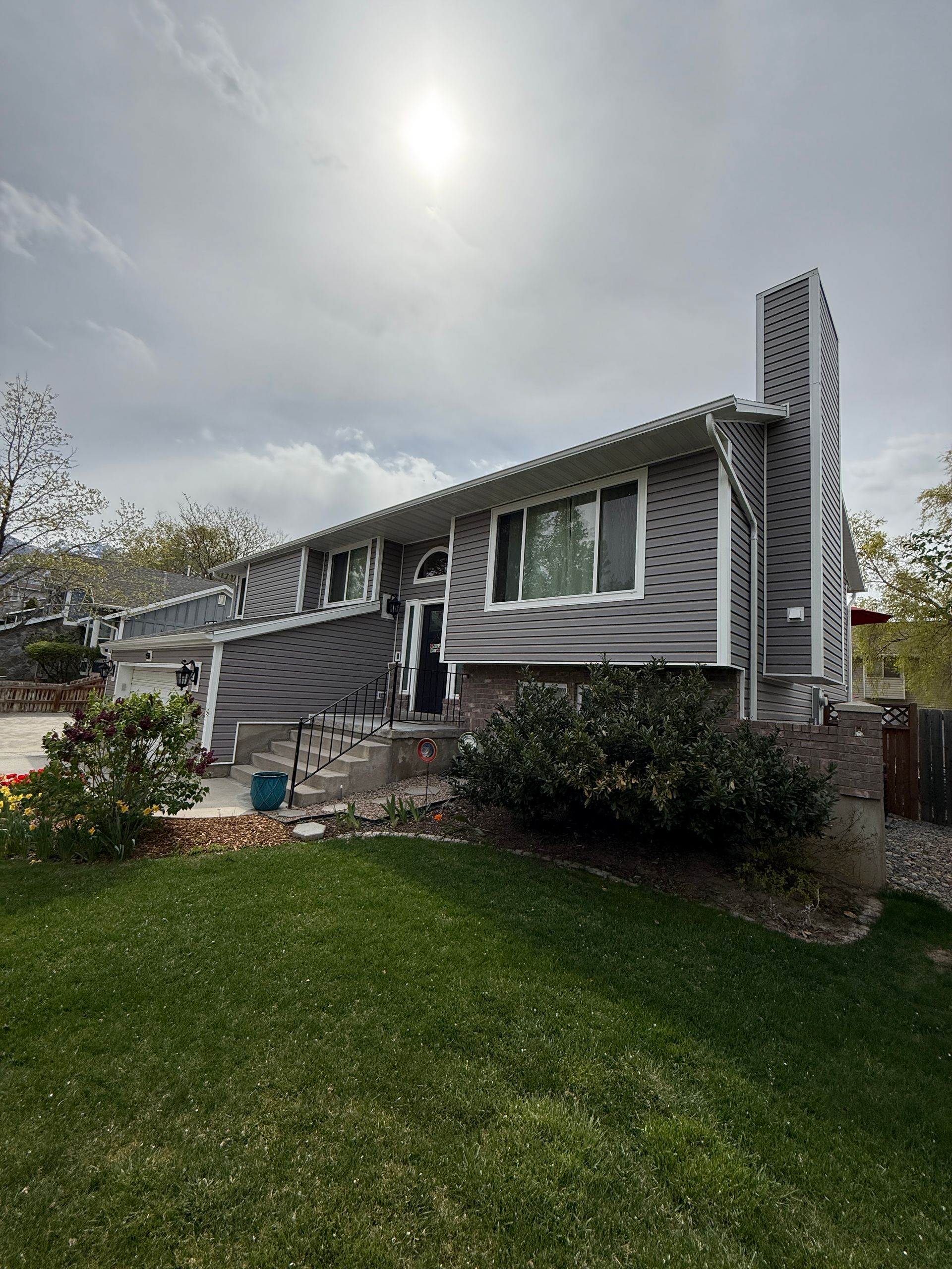 Gray house with brick base, chimney, and green lawn under a cloudy sky.