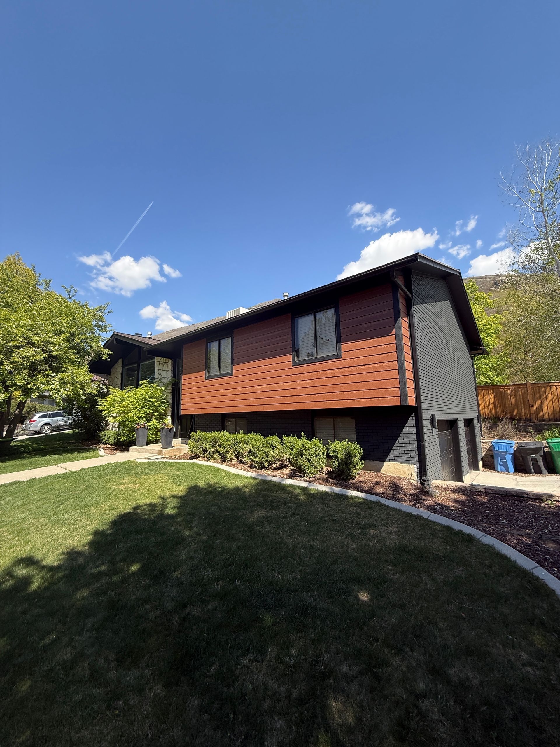 House with red brick and black siding, green lawn, blue sky.