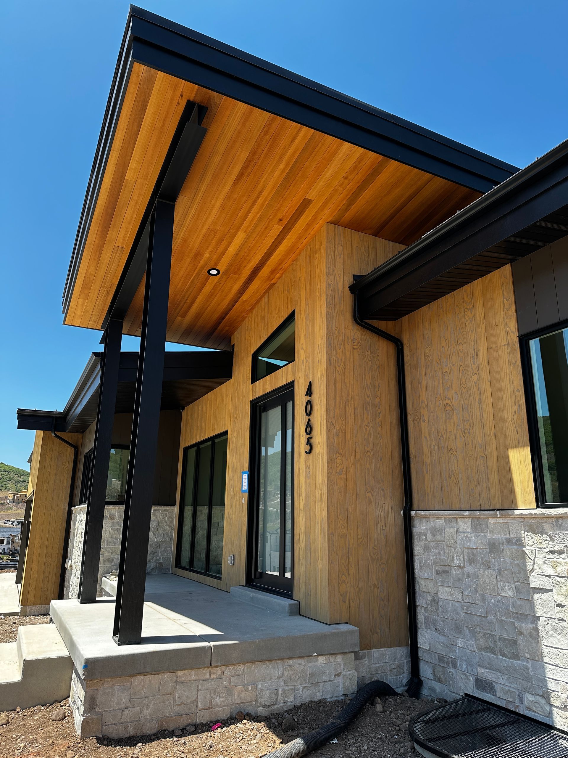 Modern home exterior with a wooden ceiling, black beams, and tan stucco walls.