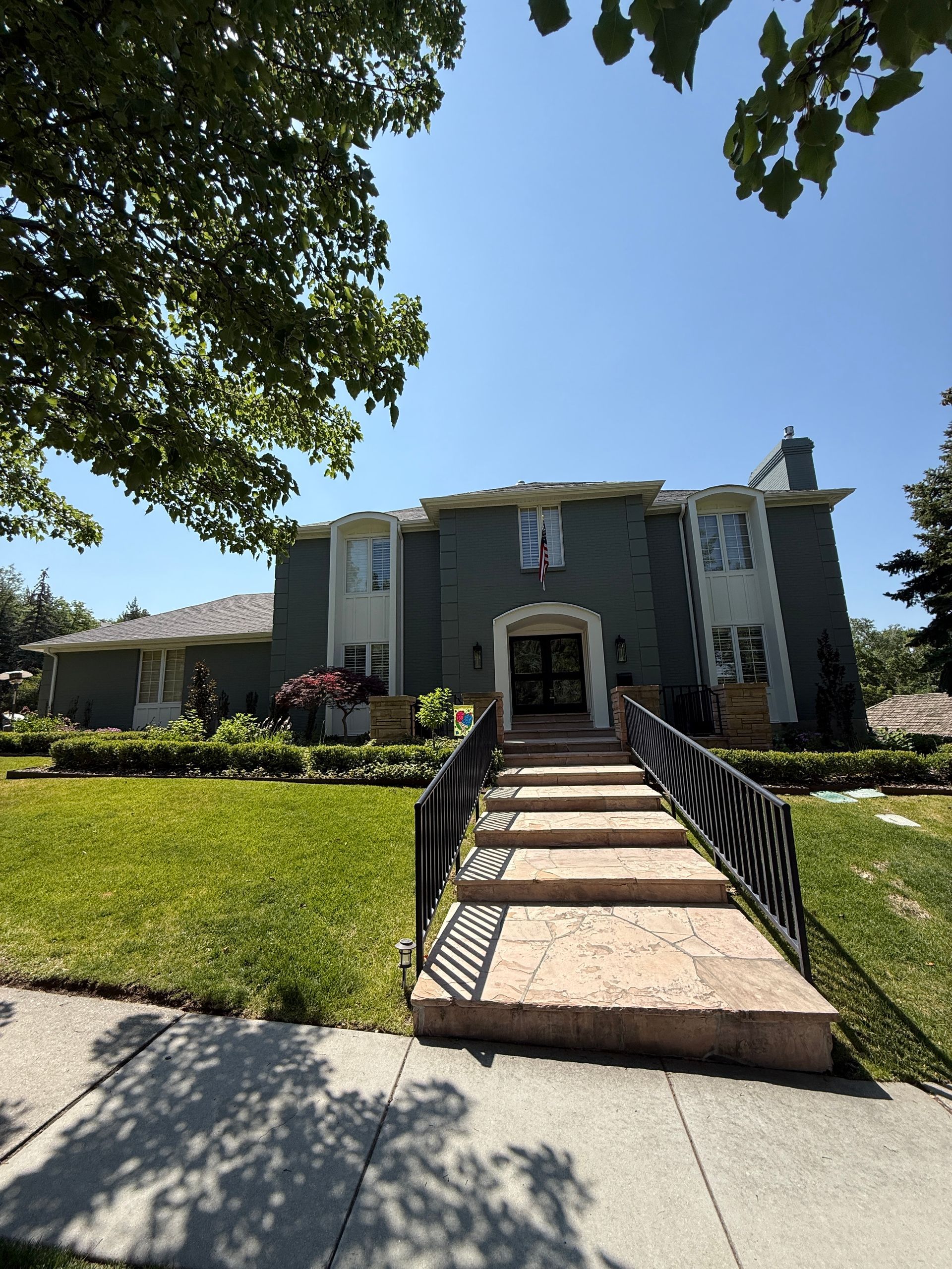 Two-story house with stone steps, green lawn, and black iron railing. Blue-green siding, white trim.