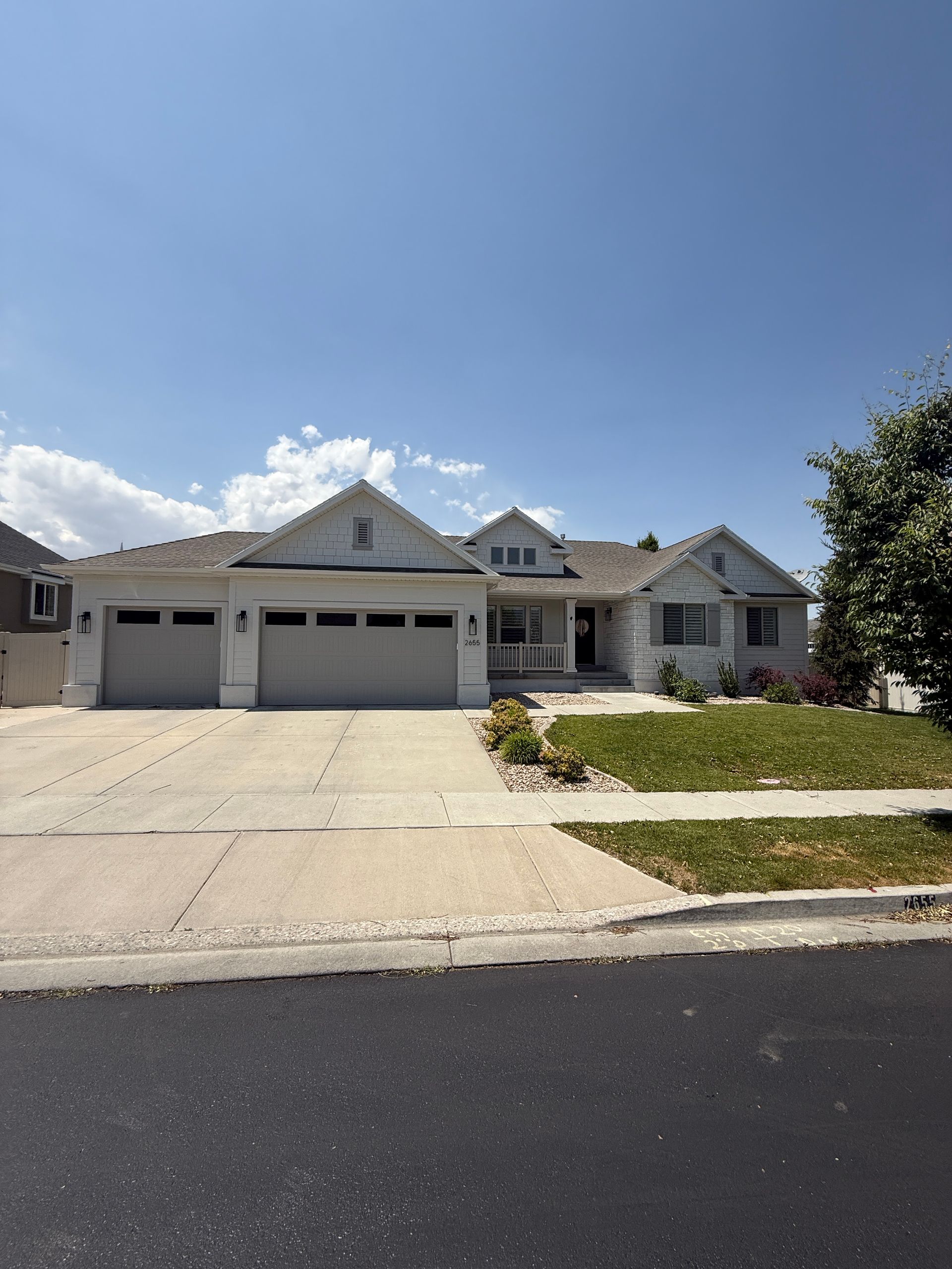 White suburban house with three-car garage, driveway, and green lawn under a blue sky.