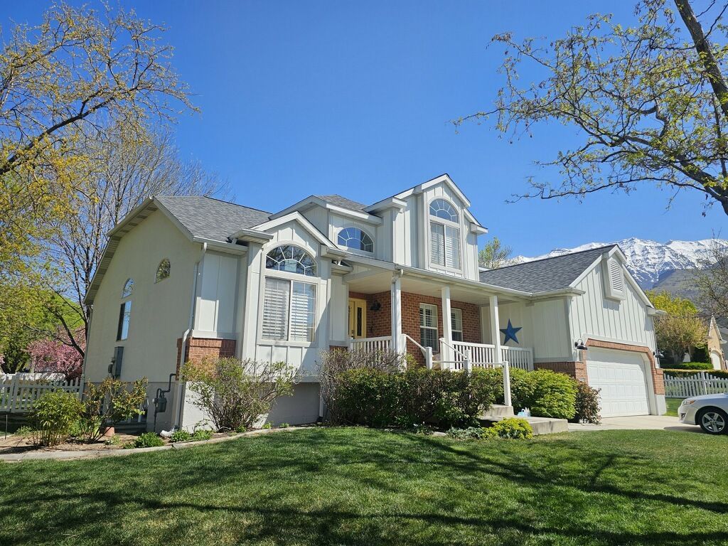 House with a white exterior, arched windows, and a porch. Mountains are visible in the background under a clear blue sky.
