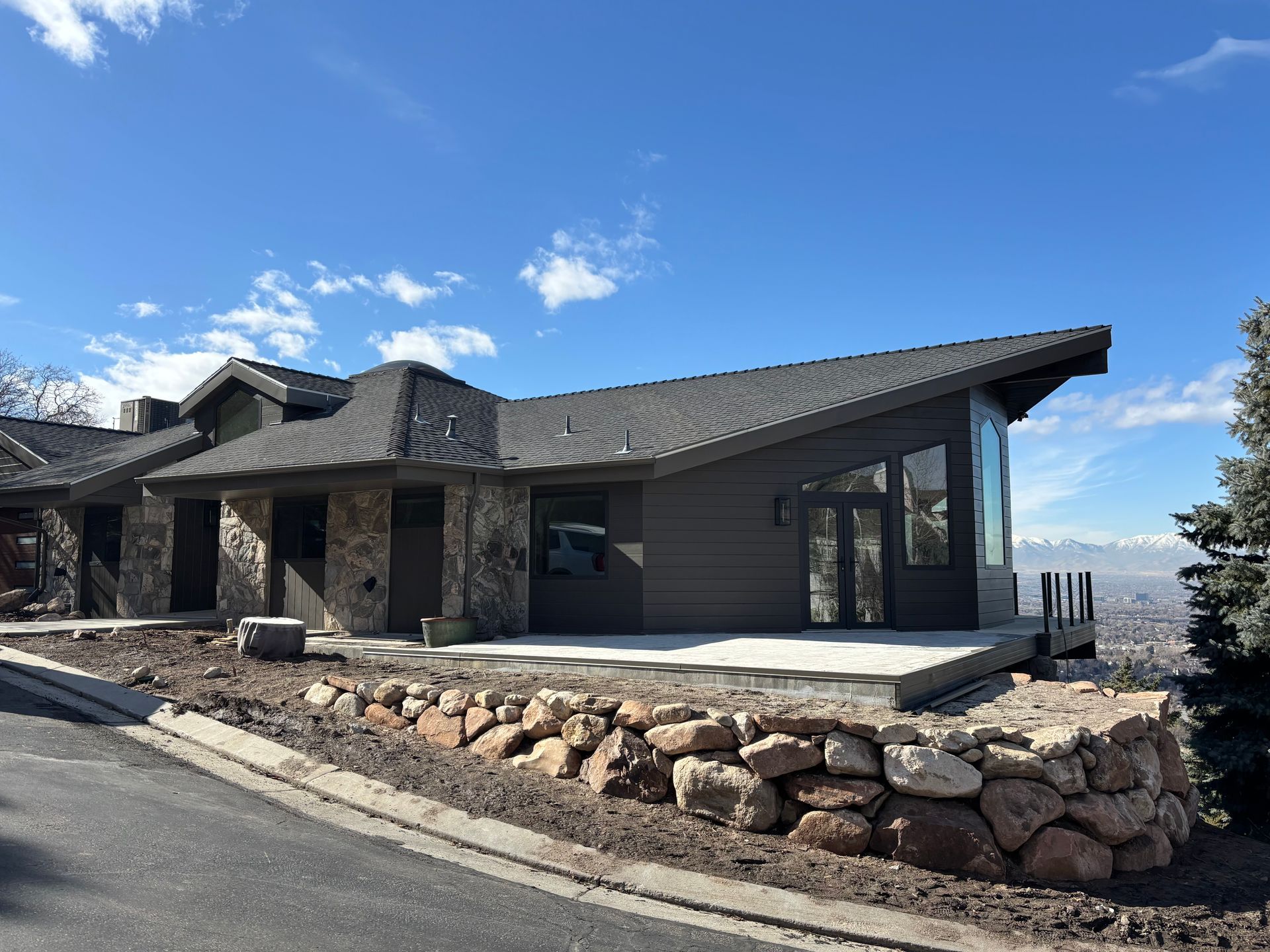 Modern home with angled roof, stone accents, and large windows on a hillside overlooking a valley.