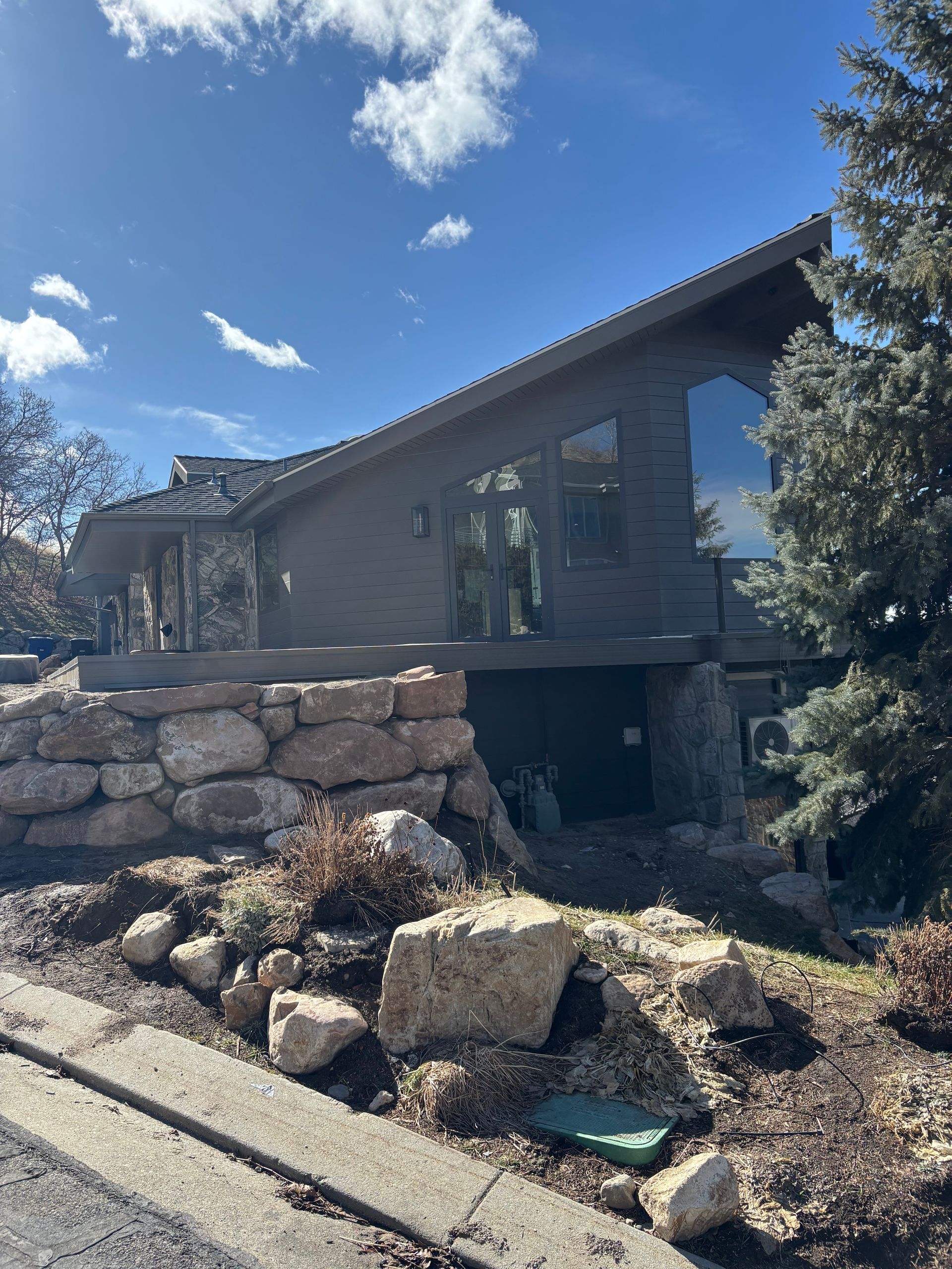 Modern house with angled roof and large windows, built on a rocky retaining wall.