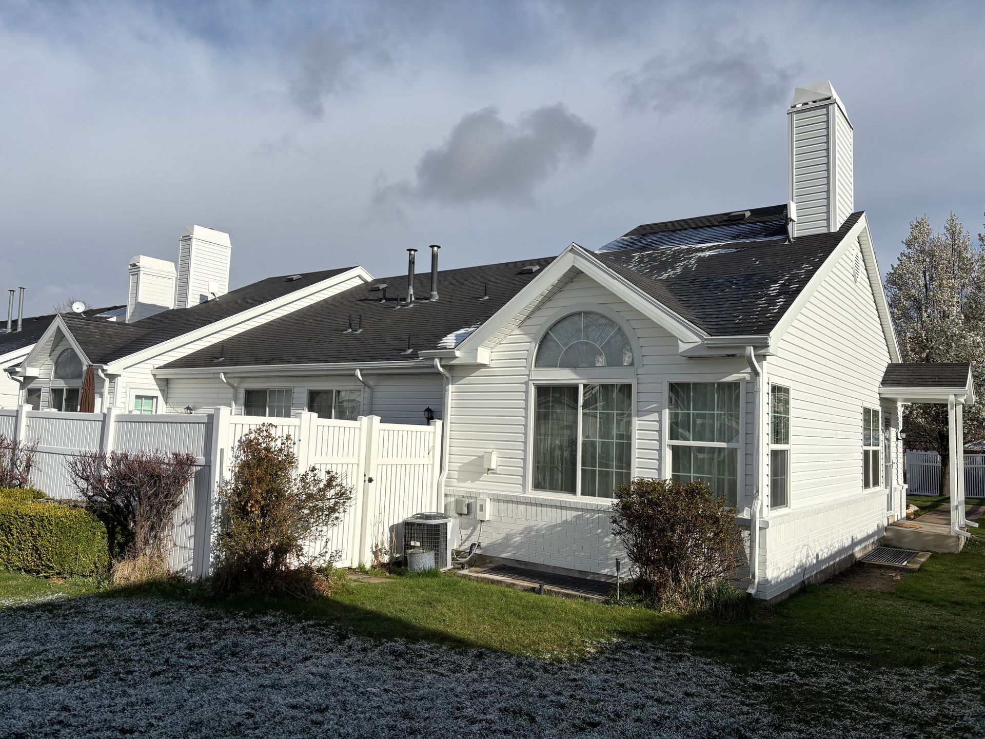 White house with black roof, white fence, and small bushes. Cloudy sky.