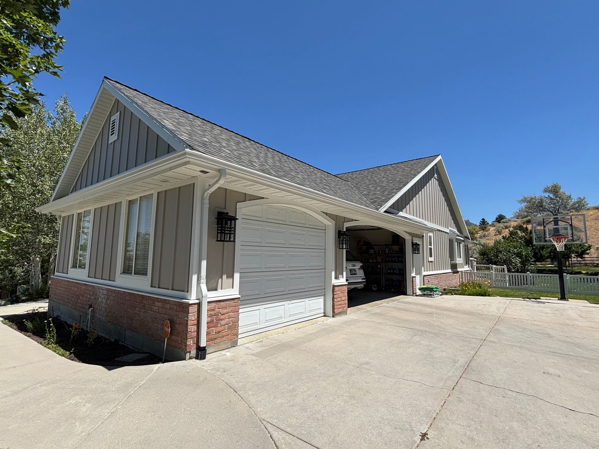 Garage with gray siding, white garage door, and red brick base under a bright blue sky.