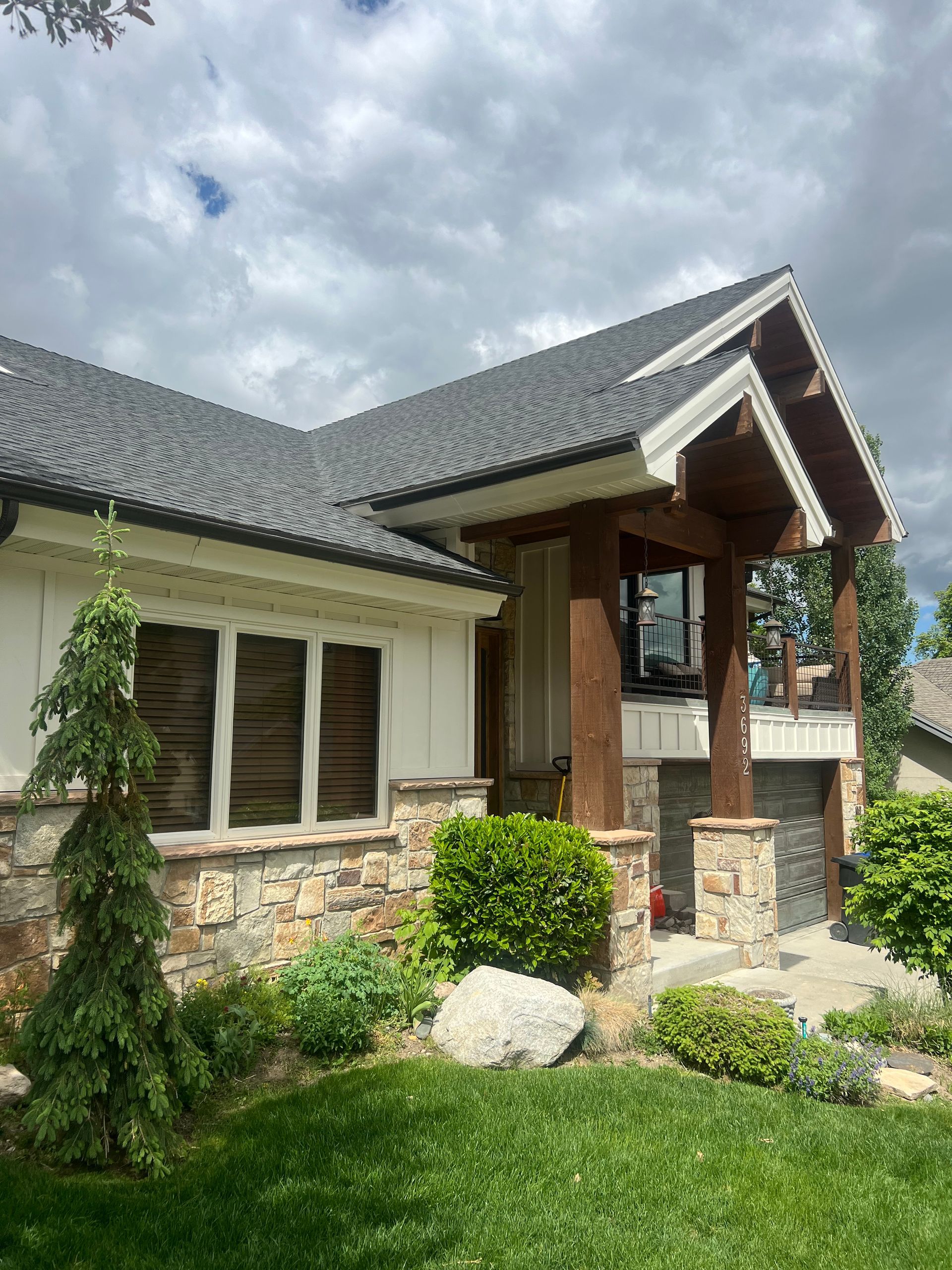 House exterior with stone and wood accents, green lawn, bushes, and cloudy sky.