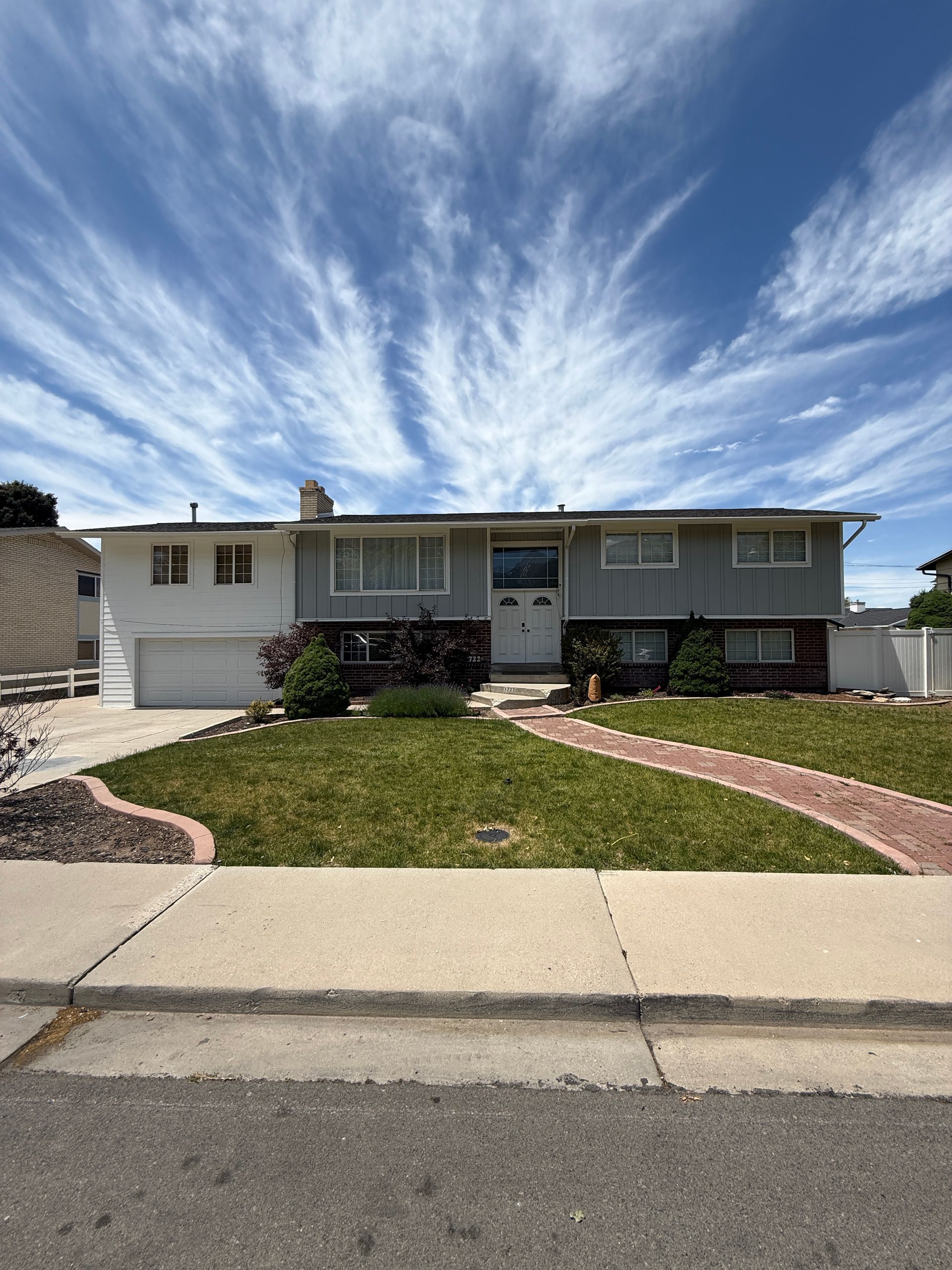 Two-story house with gray and white siding, a red brick walkway, and a blue sky with clouds.