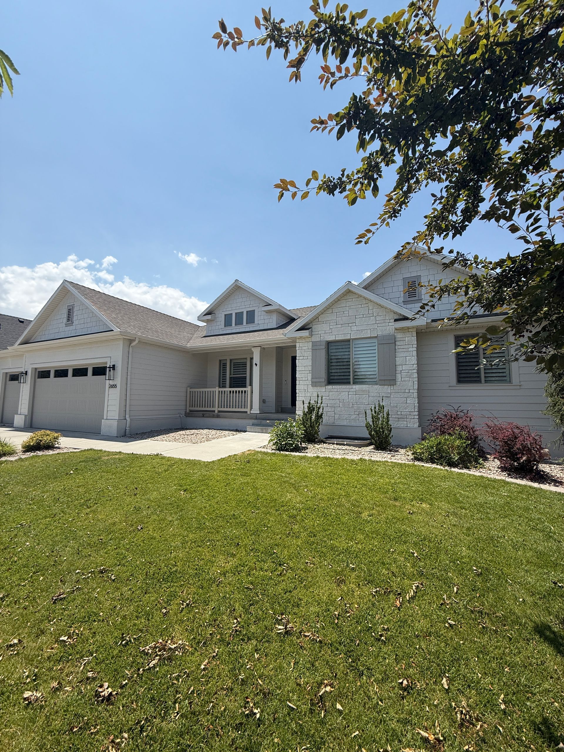 White house with green lawn, blue sky, and tree branches.