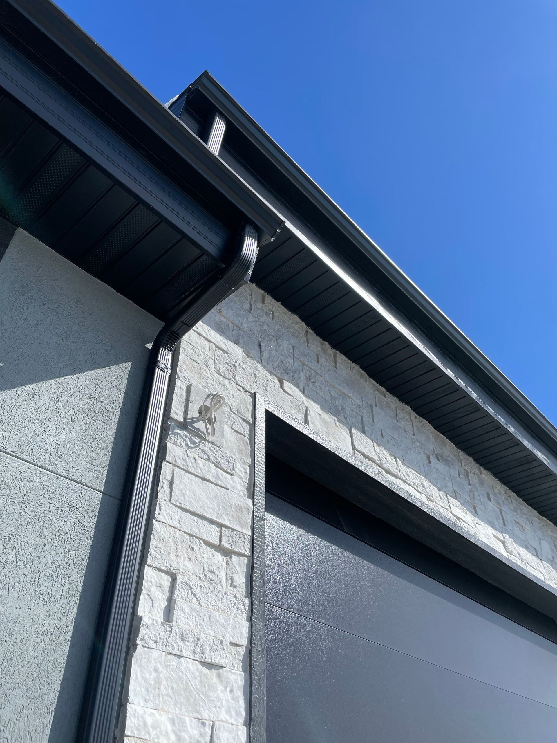 Black guttering and trim on a light-gray textured building against a blue sky.