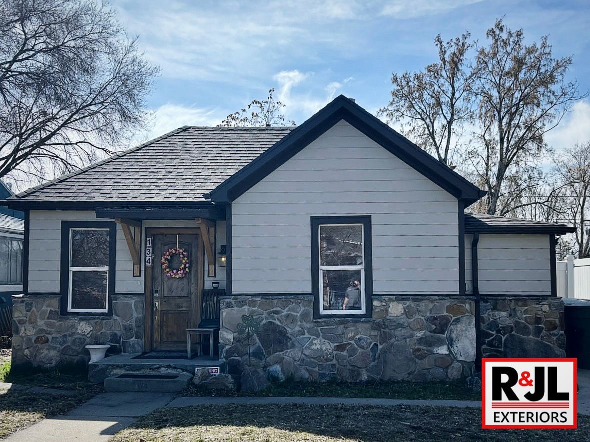 A one-story house with stone facade, gray siding, dark roof, and a wreath on the door.