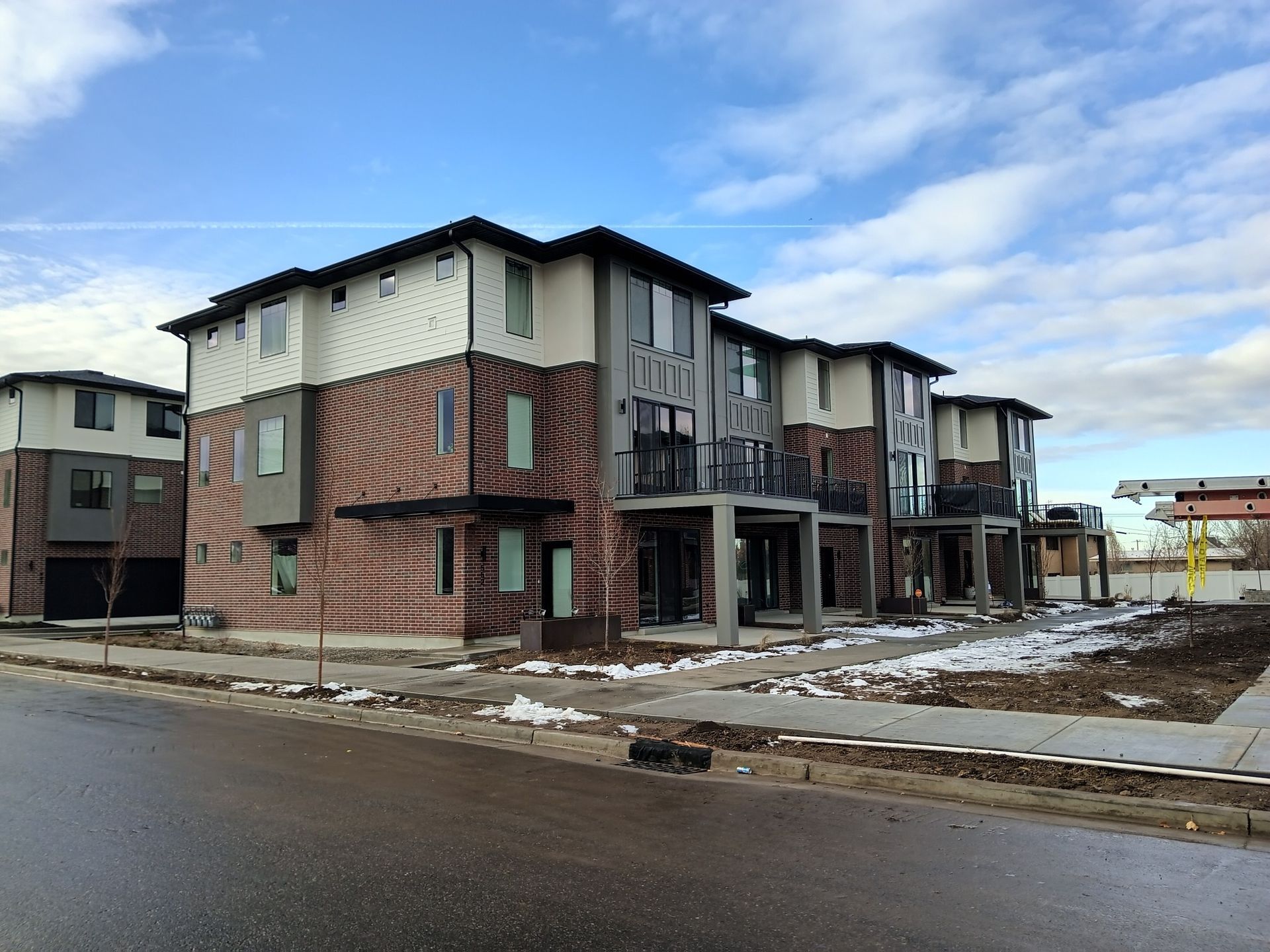 New multi-story townhomes under construction on a street with patchy snow.