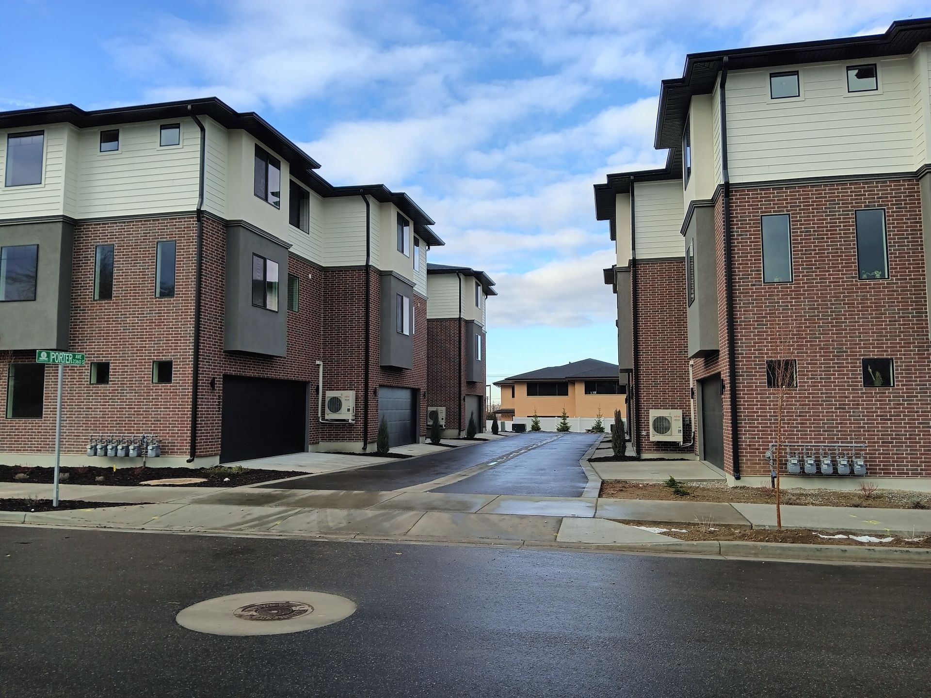Townhouses on a wet street under a cloudy sky. Buildings feature brick and gray siding.