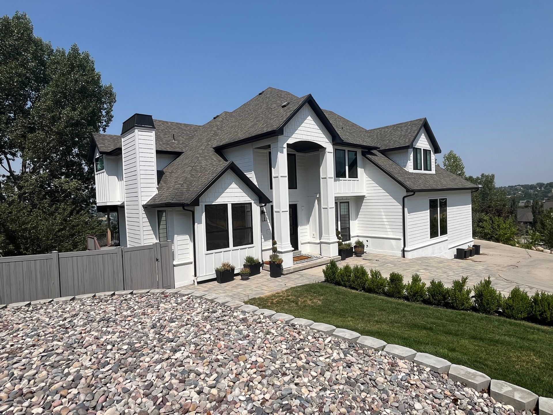 White house with black trim, gray roof, set on a hill, under a blue sky.