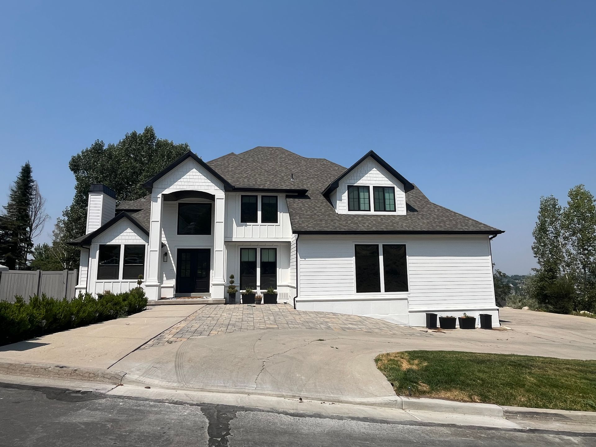 White two-story house with black trim, windows, and a dark roof. A concrete driveway leads to the house.