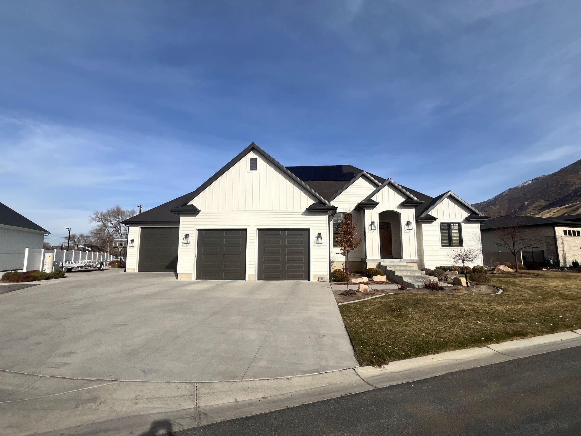 White house with a dark roof and three-car garage against a blue sky, concrete driveway.