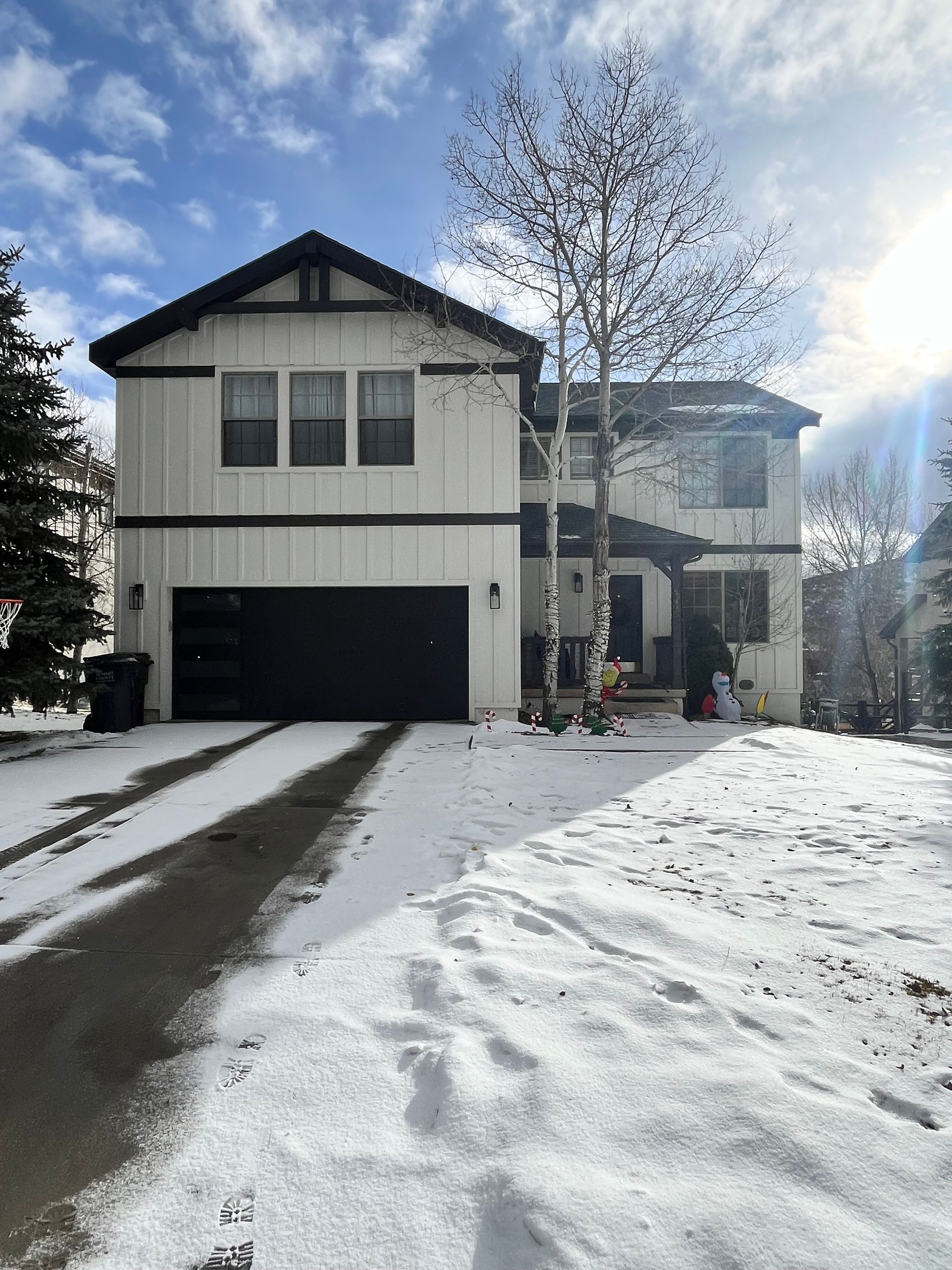 Two-story white house with black trim and garage door, snow-covered yard, sunny day.