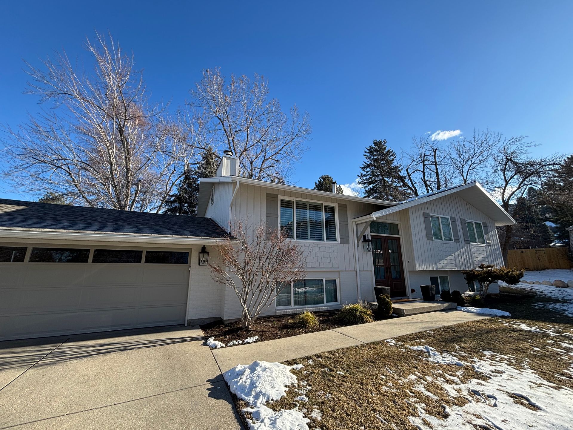 Two-story house with a white exterior, a gray roof, a garage, and snow on the ground.